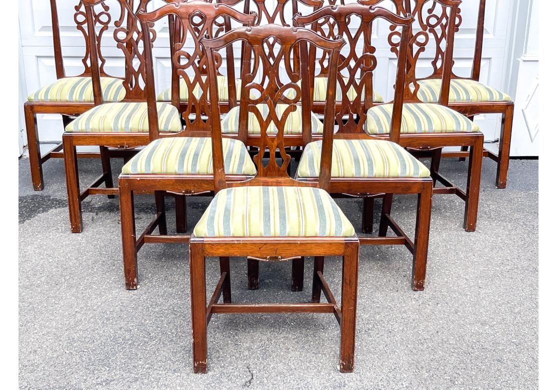 Un set di dieci sedie da pranzo in stile Chippendale dalla forma particolarmente raffinata. Ciascuna di esse si erge su gambe anteriori squadrate con gambe posteriori svasate. Con cuscini di seduta imbottiti a righe e texture e schienali intagliati