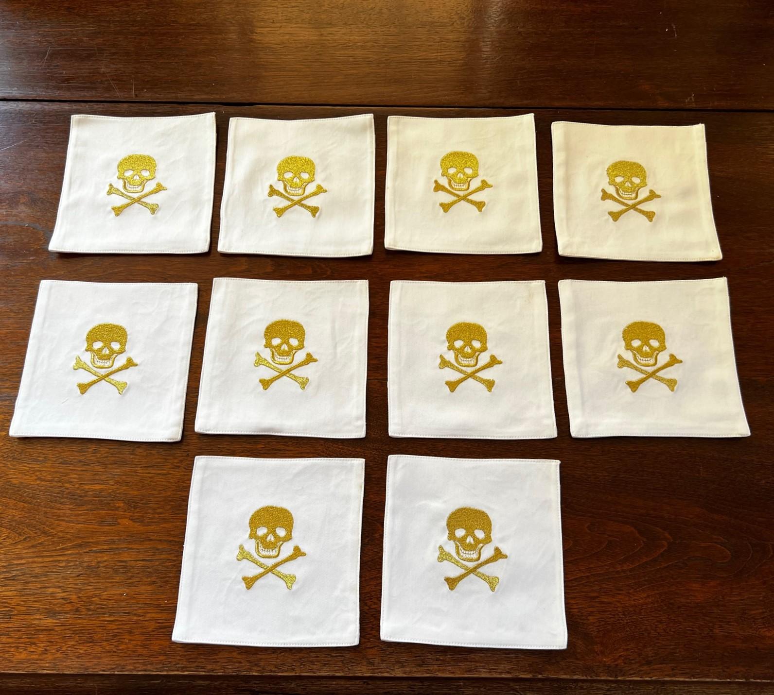 Late 20th C. a set of 10 white cotton cocktail napkins embroidered with a skull and crossbone design in a gold colored thread.

The perfect way to welcome your guests and dress up a cocktail hour. These beautiful, machine embroidered skull designs