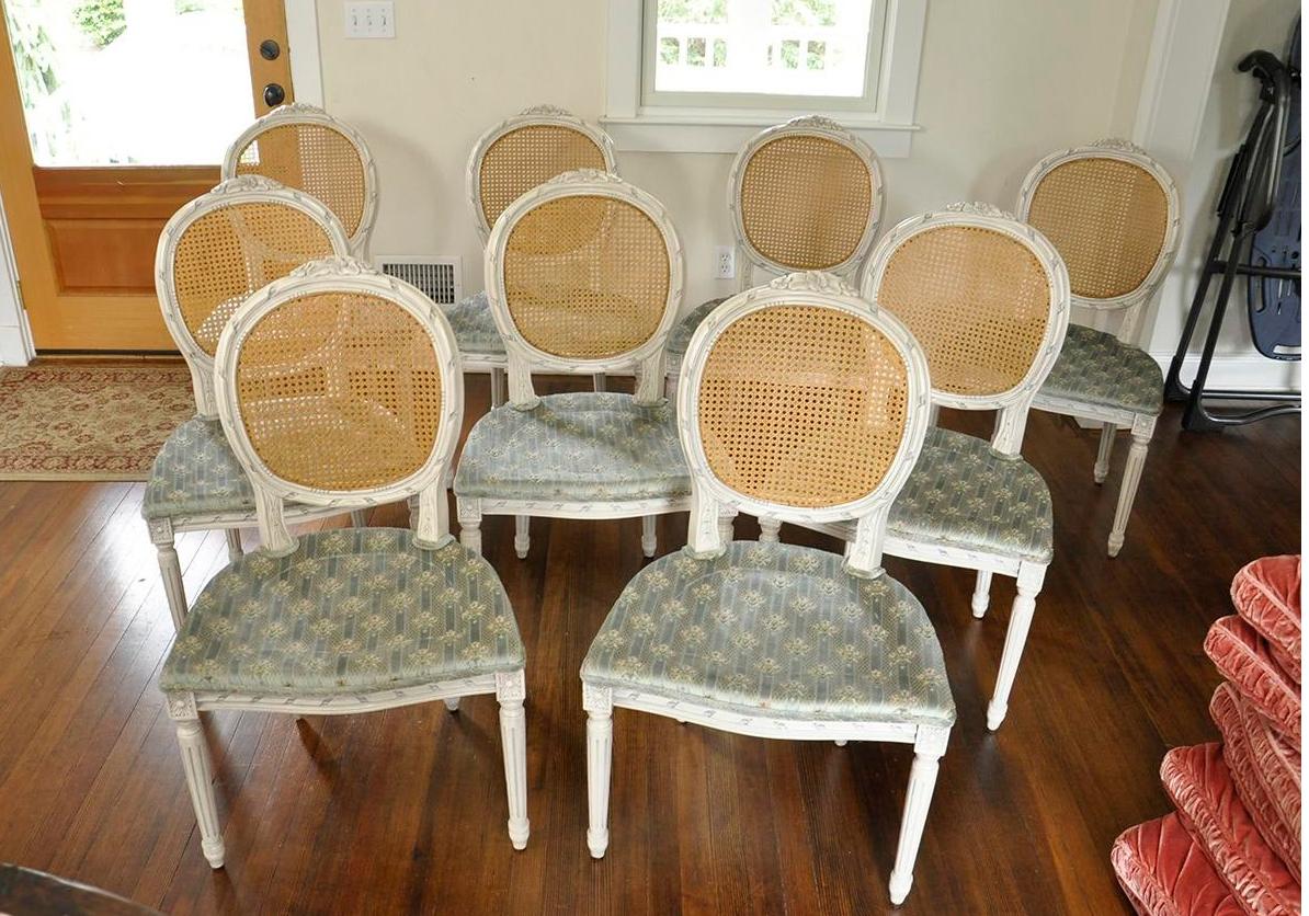 Unusual set of 10 vintage side chairs. Hand carved frame with detailed florals at the top of the back and a fluted leg all accented with additional carving throughout and painted a distressed white. The cane back is natural and in perfect condition.