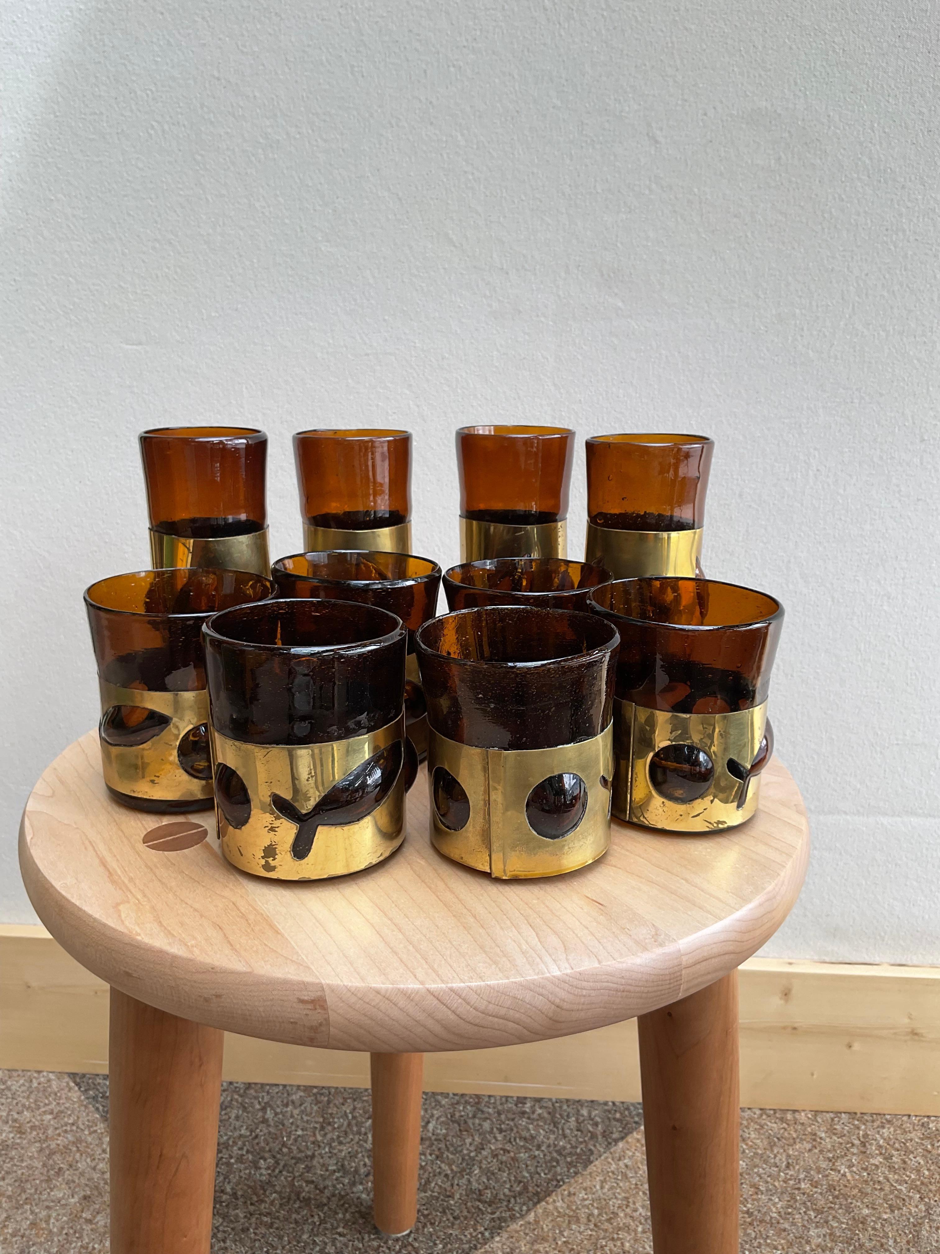 A rare and visually dynamic set of 10 handcrafted glasses by Austrian artist Felipe Derflinger. Each glass features rich amber tones paired with a removable, hand-formed brass sleeve adorned with applied sculptural motifs—alternating between