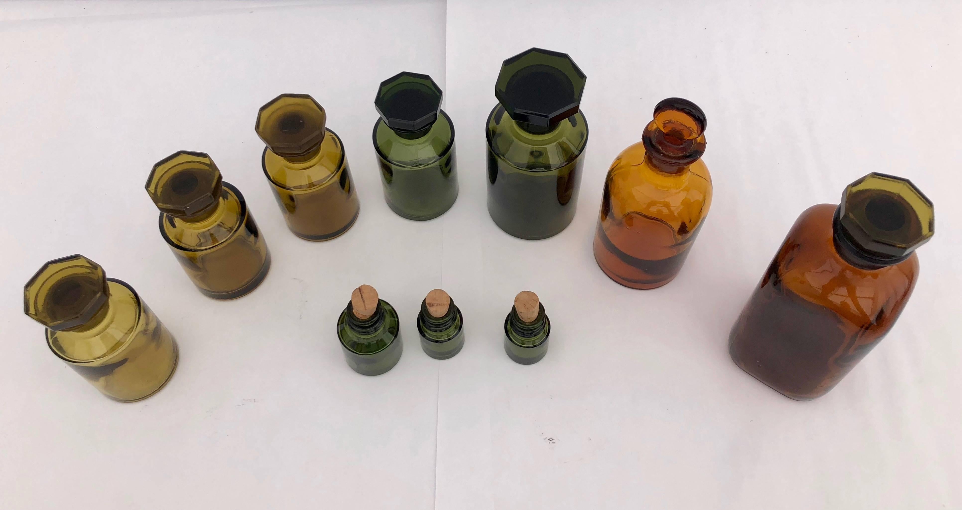 This is a set of ten French perfume-pharmacy bottles with lids, green, brown and amber.
The largest brown bottle has a square shape, while all others are round. The second largest, amber color, has a 