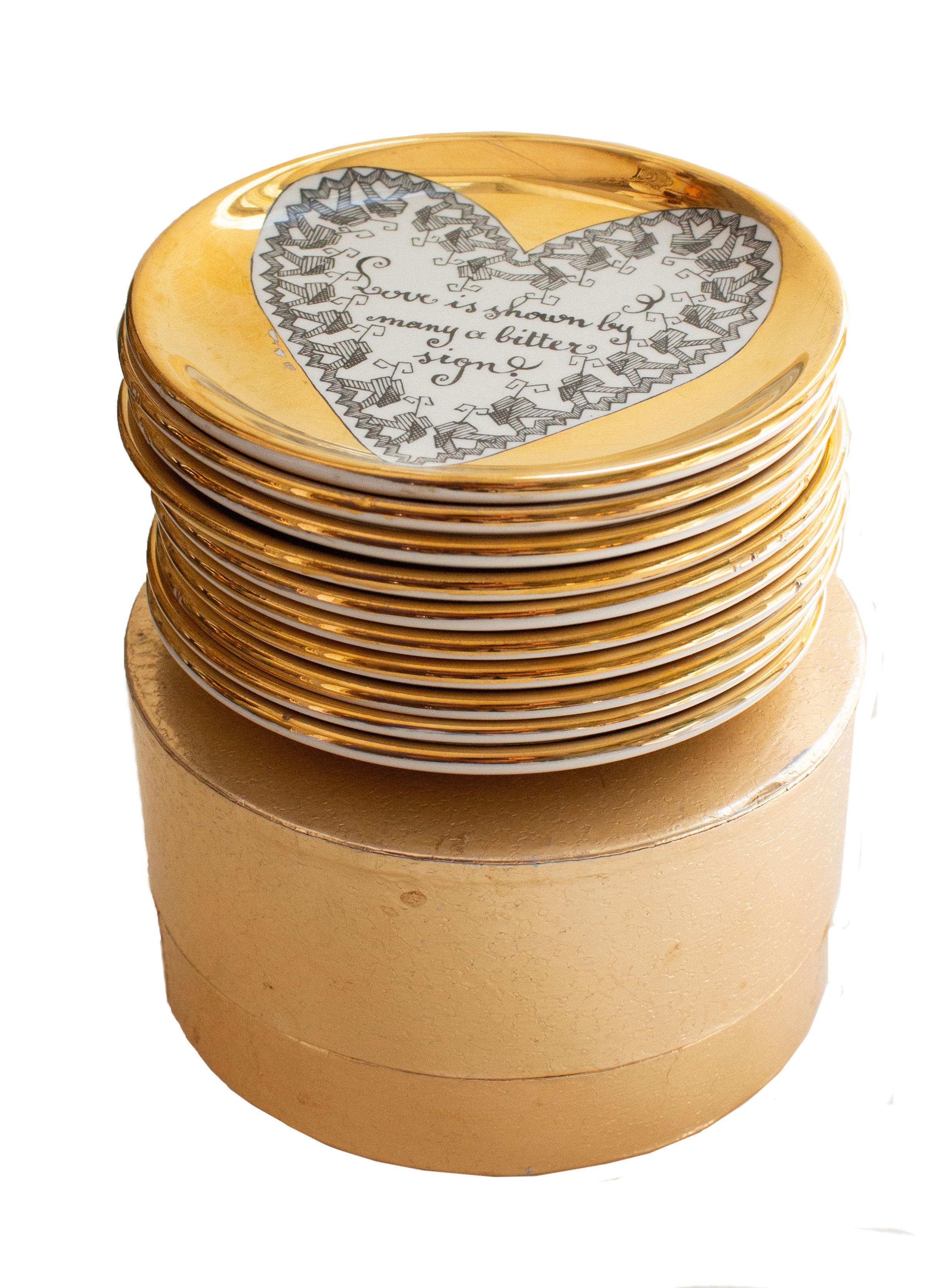 The coasters feature a central white heart set against a gold background. Inside each heart is a unique saying about love, framed by a distinct heart-shaped border. The set includes its original gilded box and contains 10 coasters in total, with 4