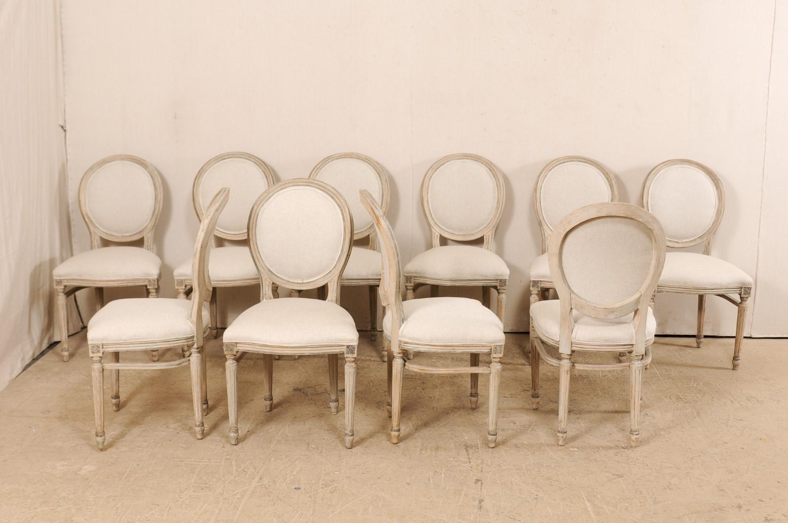 A set of 10 Louis XVI style American oval-back upholstered side chairs. This set of vintage chairs have been carved in the typical manner of the Louis XVI period, with the rosettes adorning their knees, and presented upon round, fluted legs which