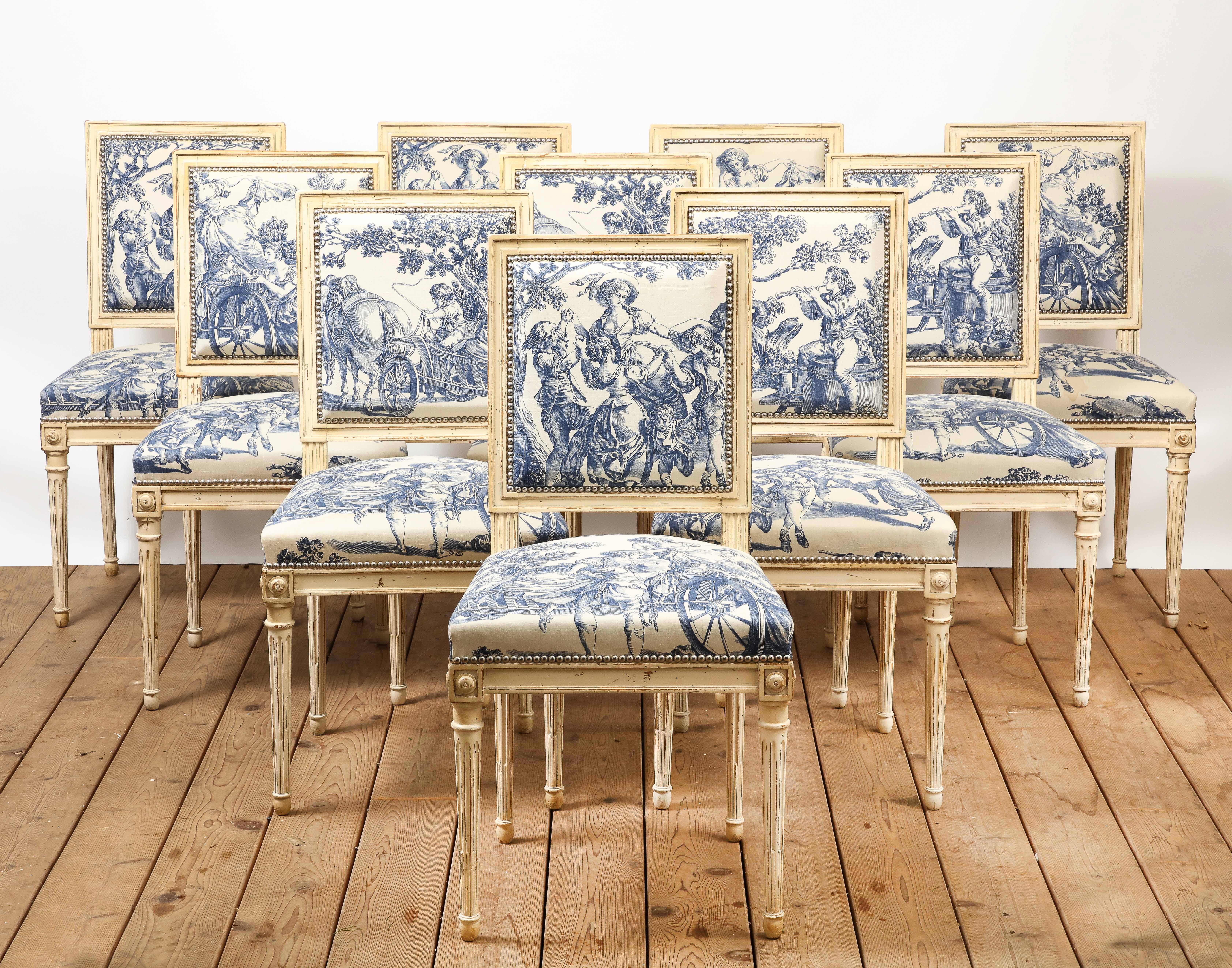 Set of 10 Louis XVI style French dining chairs. The carved wood frames are painted cream, upholstery is blue and white toile, adorned with silver nail heads. Condition as shown. 