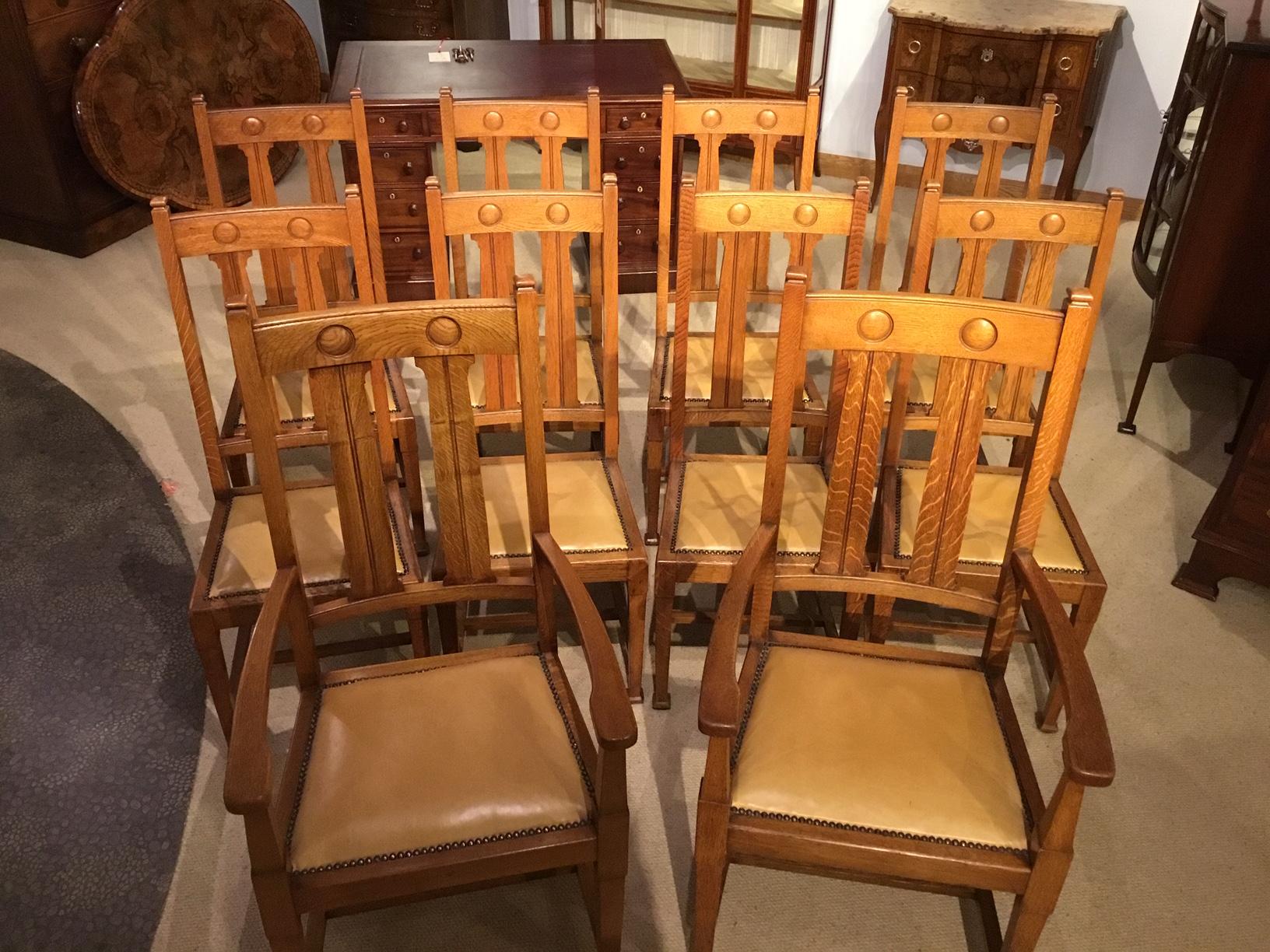 A Good set of 10 oak Arts & Crafts period dining chairs by Shapland & Petter of barnstaple. The shaped top rail with incised roundels, vertical splats and having leather covered seats with brass studded detail. Supported on square tapering supports