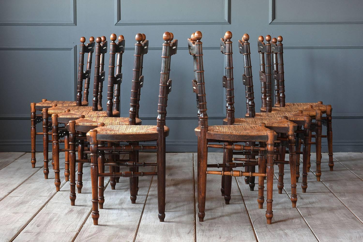This set of ten 1900s French Provincial-style dining room chairs feature a solid walnut wood frame with the original finish. The frame has a ladder back with turned wood details on the legs and back supports. The chairs are finished with rush seats