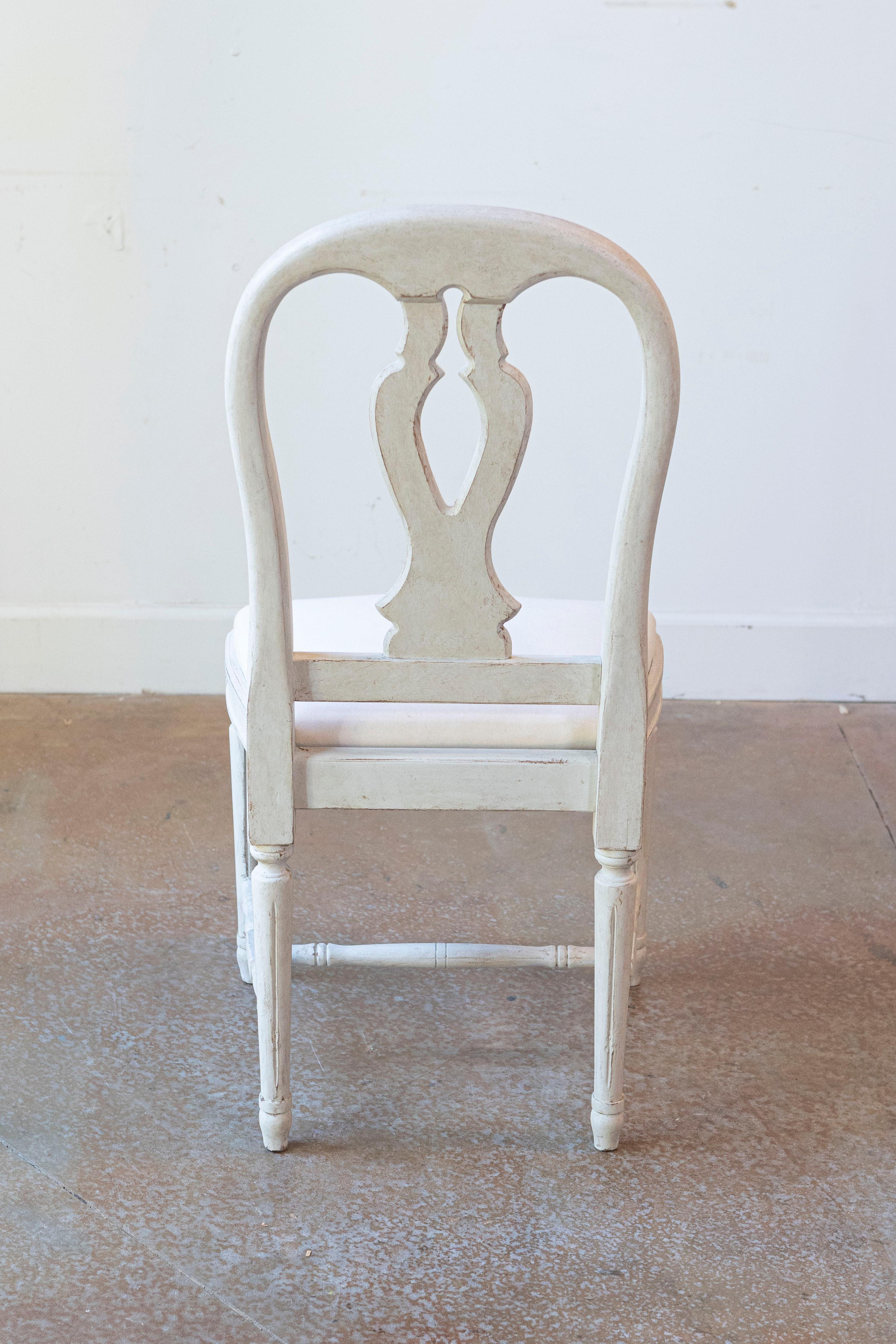 Un set di 10 sedie da sala da pranzo in legno dipinto di Wood dell'inizio del XX secolo, con stecche intagliate, gambe scanalate e tappezzeria bianca nuova. Creato in Svezia durante la fine del secolo, questo set di 10 sedie laterali è