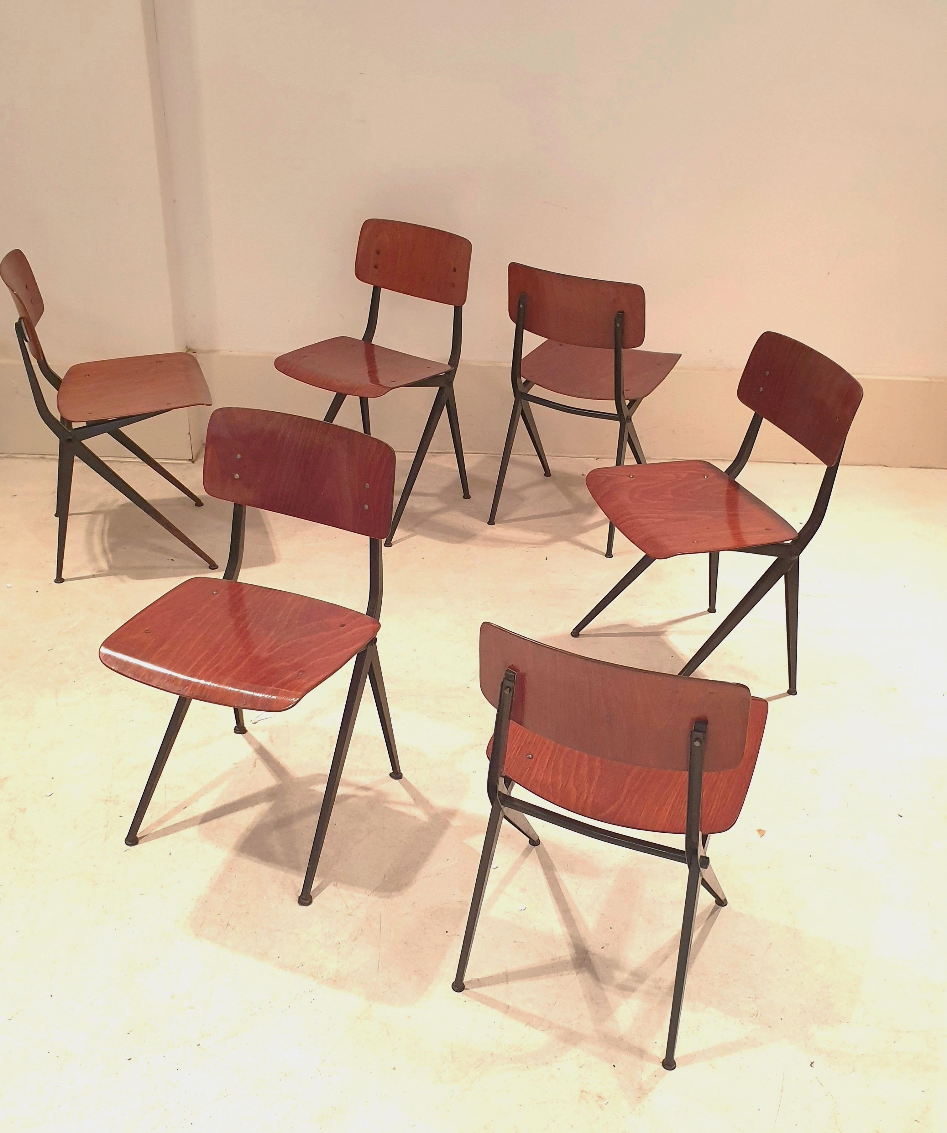 Ensemble de 6 chaises de style industriel par Marko Holland. Ces chaises utilitaires confortables ont de belles assises et dossiers en teck vieilli et des piétements minimalistes en métal laqué noir. Leur simplicité leur permet de s'intégrer dans