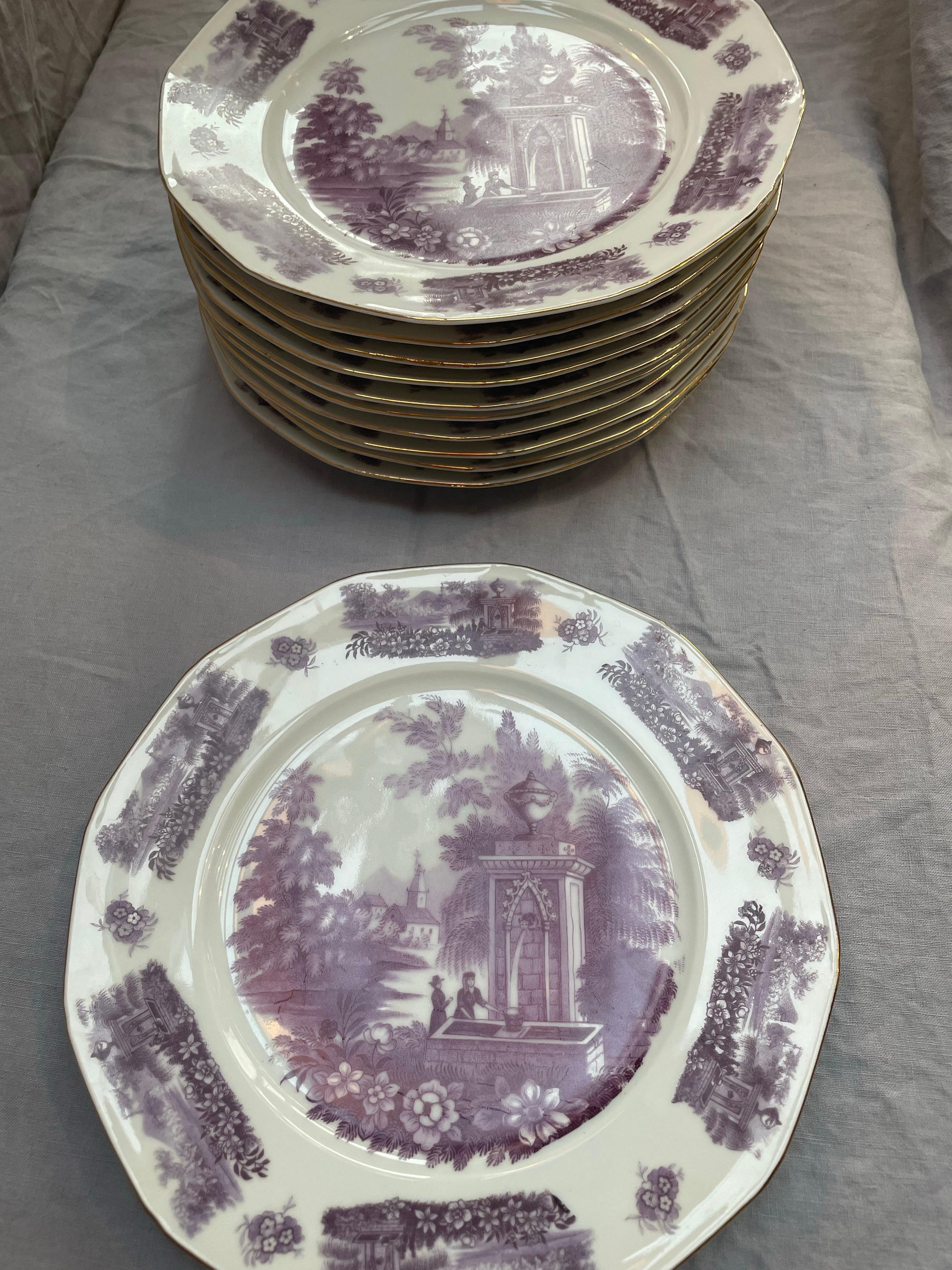 A refined set of eleven octagonal Czech porcelain plates, each decorated in a delicate lavender-to-plum transferware scene depicting a romantic garden fountain with figures and architectural details, framed by lush floral vignettes. The design is