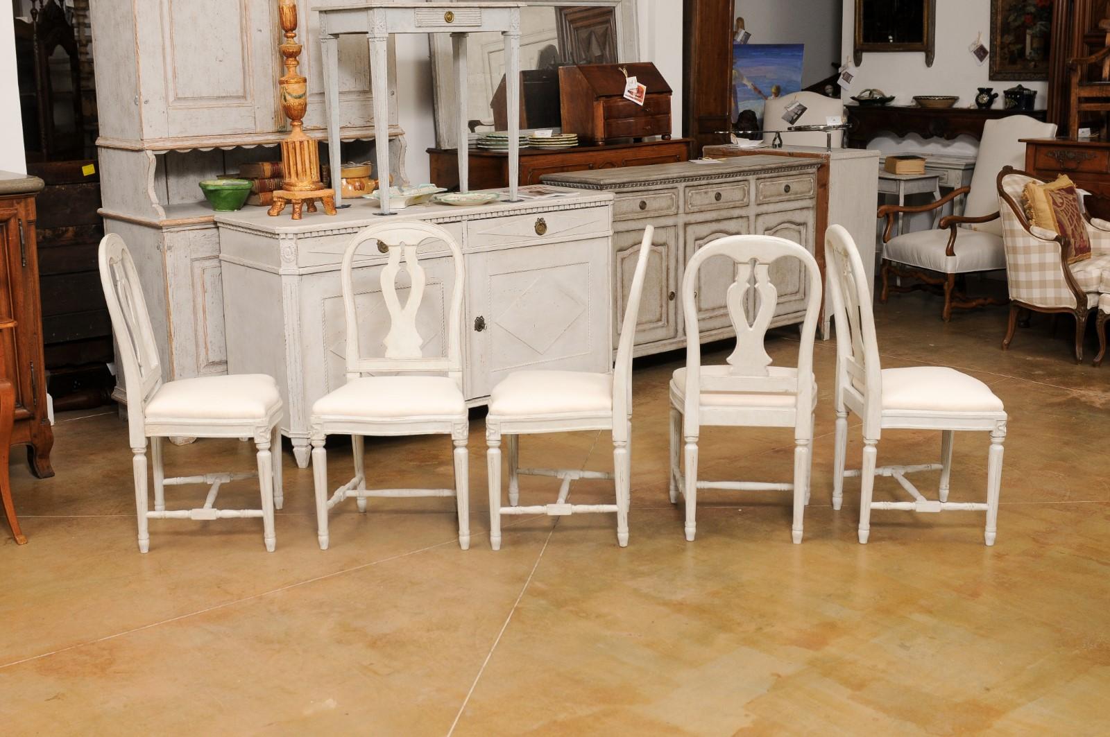 A set of 11 Swedish painted wood dining room chairs from the early 20th century, with carved splats, fluted legs and new white upholstery. Created in Sweden during the Turn of the Century, each of this set of 11 side chairs features a balloon style
