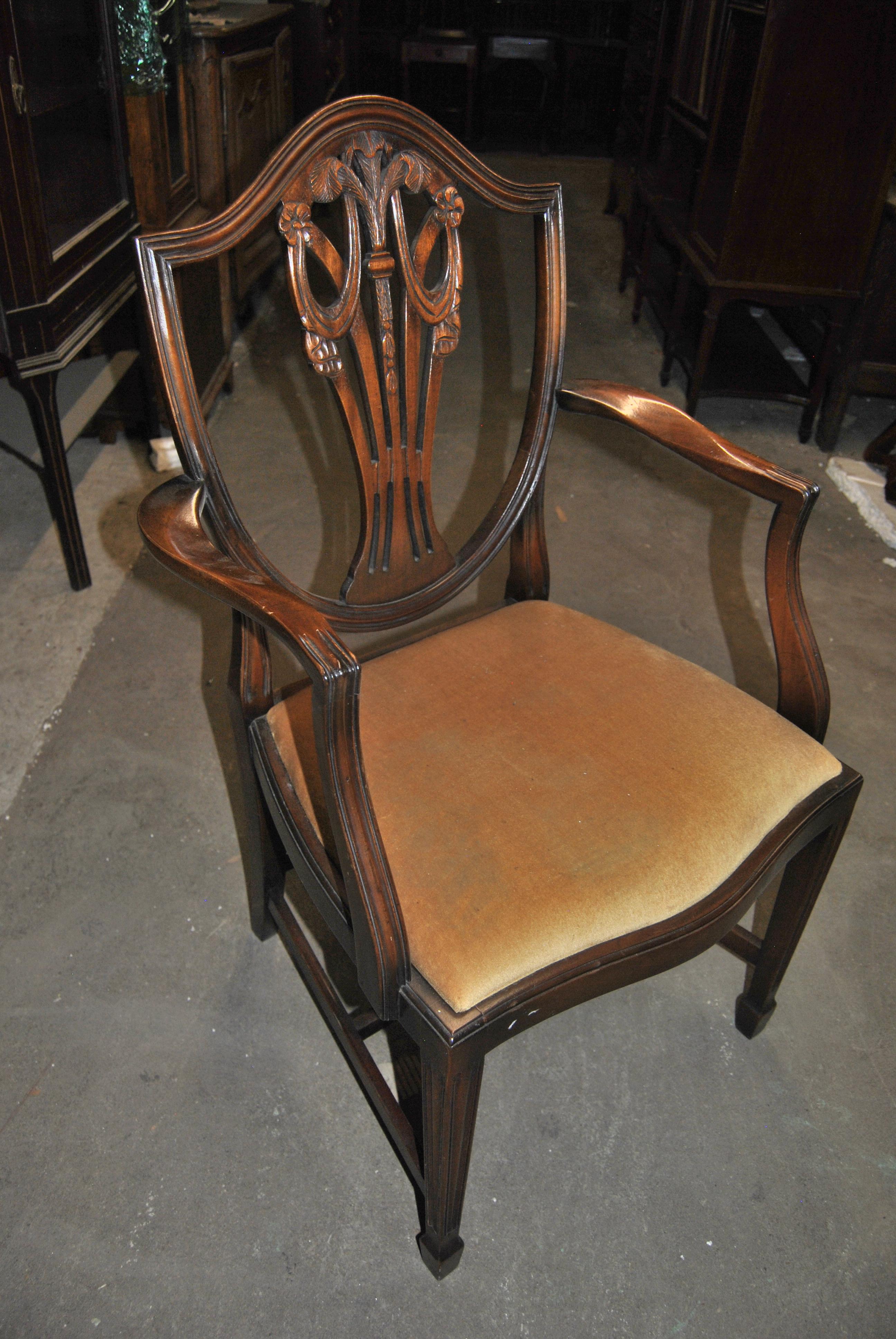 This is a matched set of 12 solid mahogany Hepplewhite style shield back chairs made in England, circa 1950. The set consists of 2 arm chairs and 10 side chairs. They have a beautifully shaped Shield Back with reeded molding. Each is all hand carved