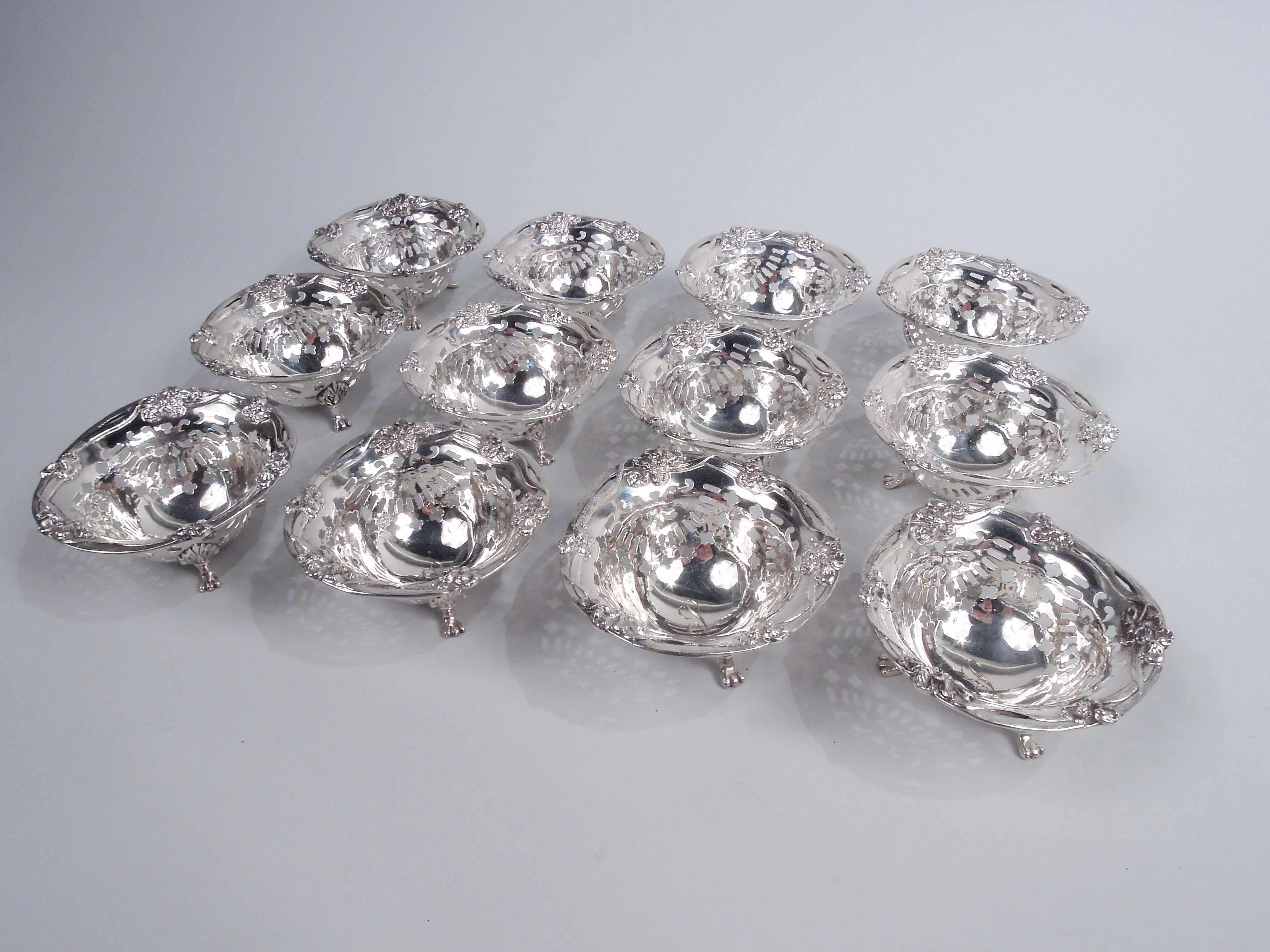 Set of 12 Art Nouveau sterling silver nut dishes. Made by Howard Sterling Co. in Providence, ca 1900. Each: Round and pierced with 3 leaf-mounted paw supports. Cast and open tendril rim with flower heads. Well has engraved single-letter monogram.