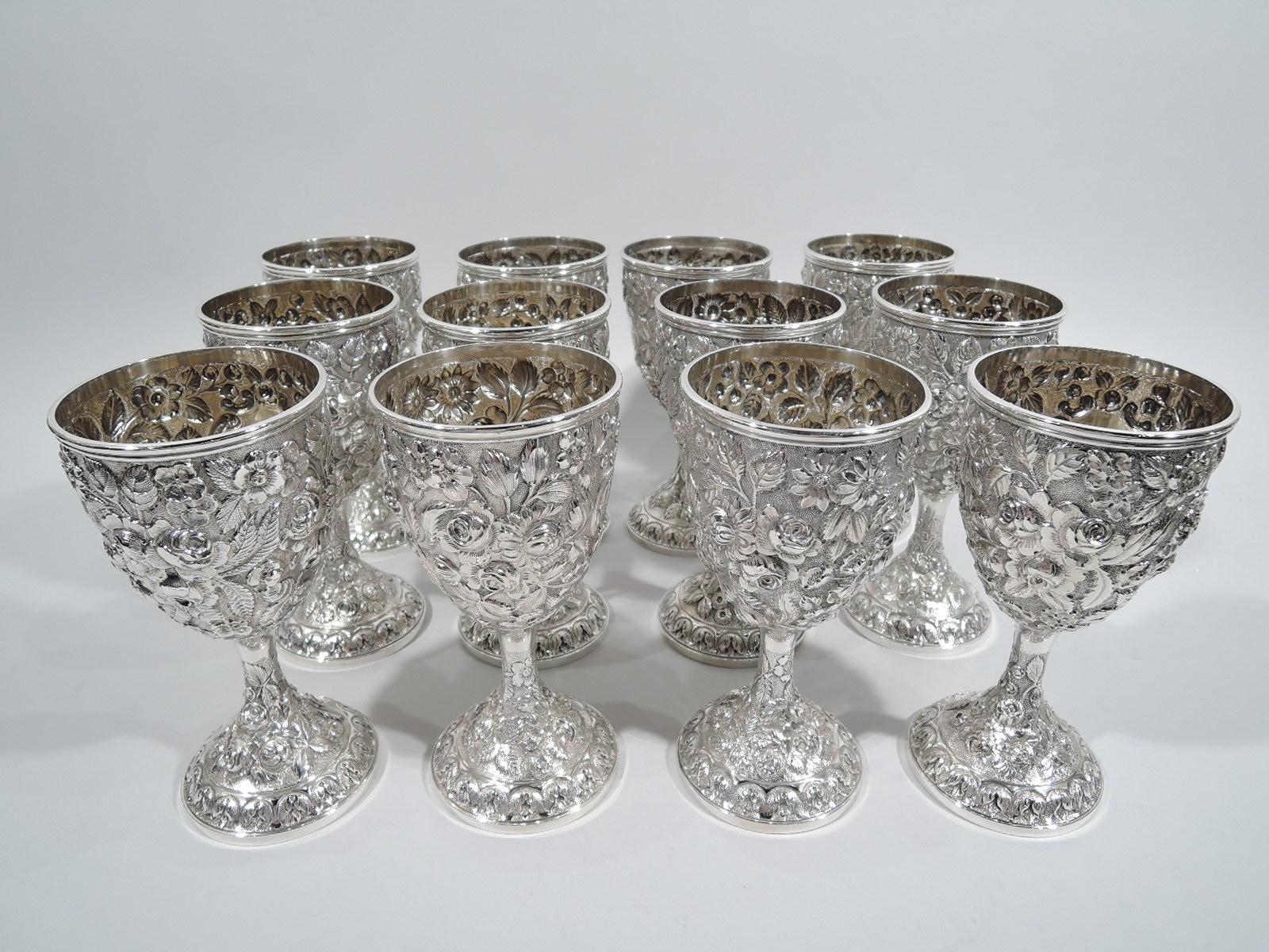 Set of 12 turn-of-the-century sterling silver goblets. Each: Oval bowl on cylindrical support flowing into raised foot. Floral and foliate repousse on stippled ground. Bowl has plain cartouche (vacant) in scrolled frame. Interior gilt washed. Pretty