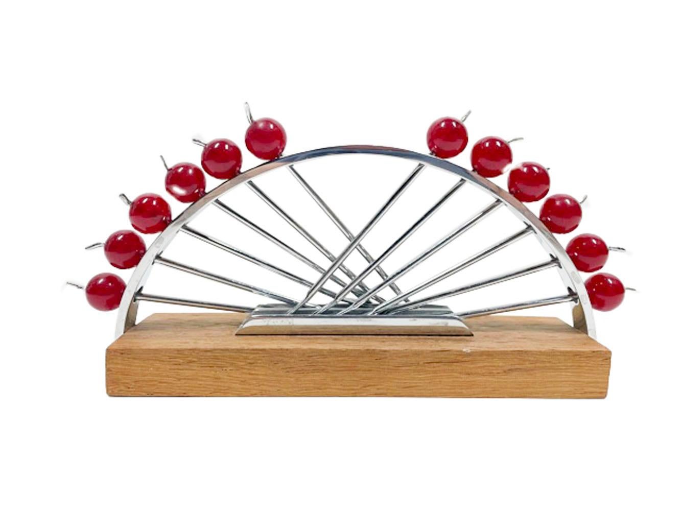 Set of 12 Art Deco forked cocktail picks of chromed steel with red Lucite cherry red apple form tops held in a chromed arc on a rectangular wood base.