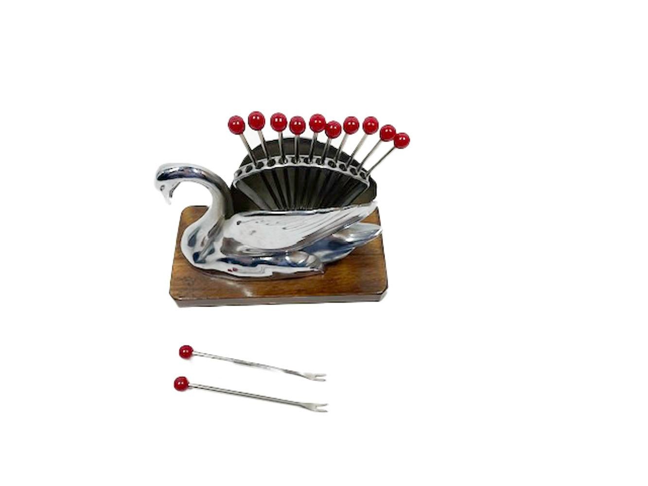 Art Deco chromed metal swan on rectangular wood base holding 12 forked chromed steel and cherry red Lucite cocktail picks between its wings.