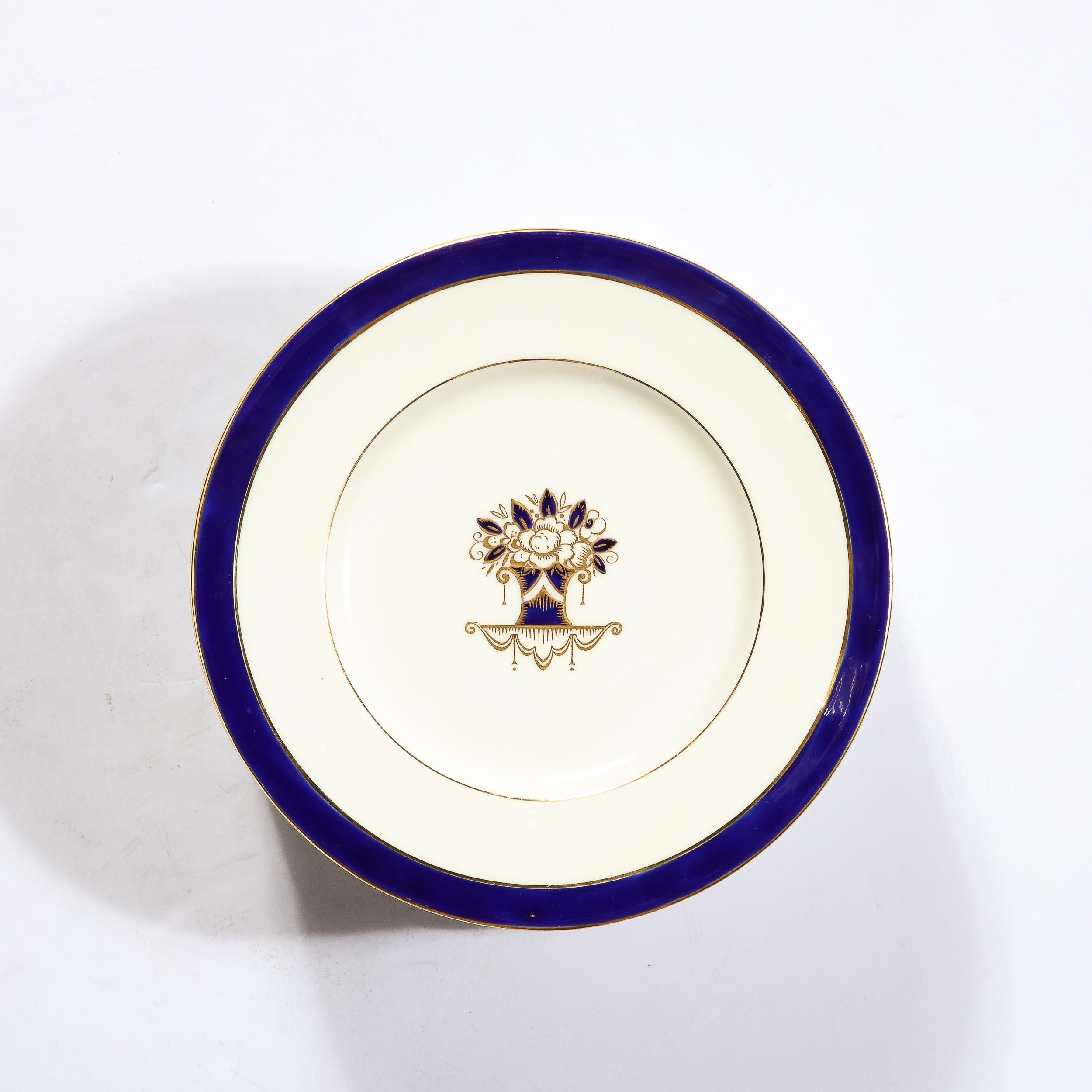 This elegant set of 12 Art Deco plates were realized by Minton for the esteemed American luxury maker Tiffany in England circa 1930. They feature circular bodies with subtly raised cobalt borders and gilded perimeters. The cream interior of each