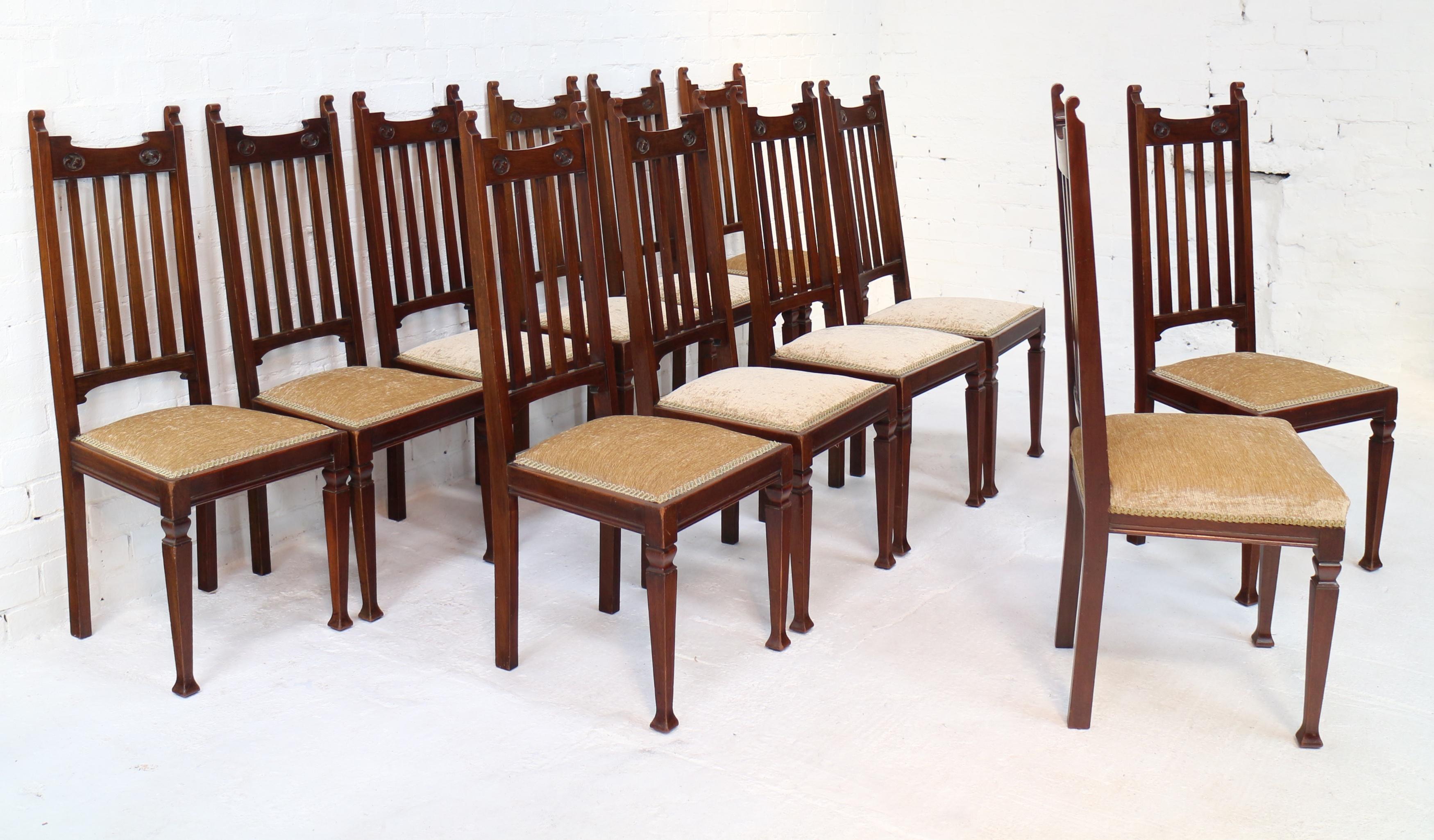 An attractive set of 12 Arts & Crafts/Art Nouveau walnut high back dining chairs attributed to Shapland & Petter and dating to circa 1880. With scroll ears and shaped toprail carved with acanthus roundels above similarly shaped bottom rail with four