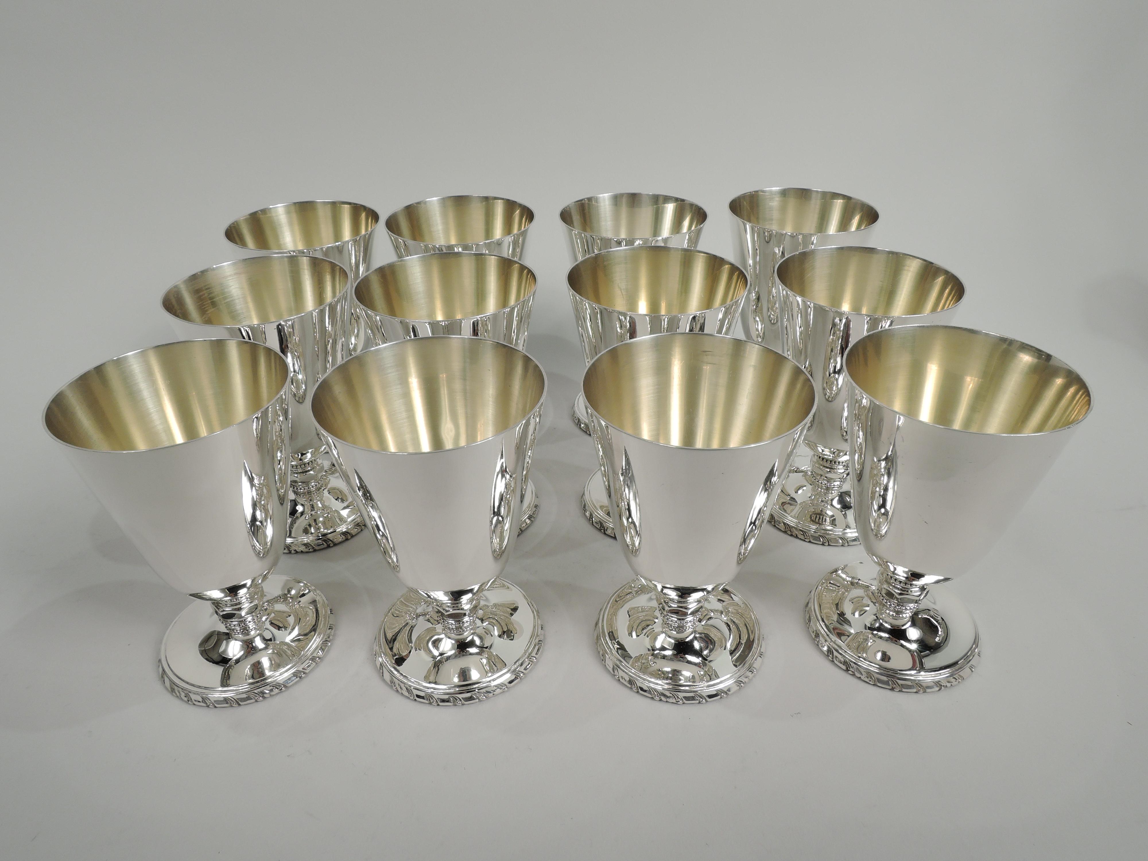 Set of 12 Mid-Century Modern Classical sterling silver aperitif cups. Retailed by Cartier in New York. Conical bowl on short stem with faceted knop between beaded bands; foot gently raised with gadrooned rim. Bowl interior gilt washed. Fully marked