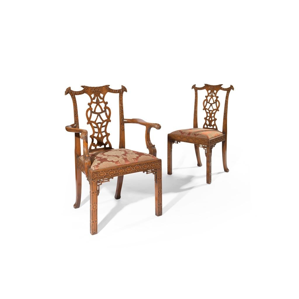 An Edwardian set of 12 Chinese Chippendale style pine and beech dining chairs, circa 1920. Comprising 4 armchairs and 8 side chairs, each with a serpentine top rail with parchment scroll carved ears. With pierced and carved interlaced splats