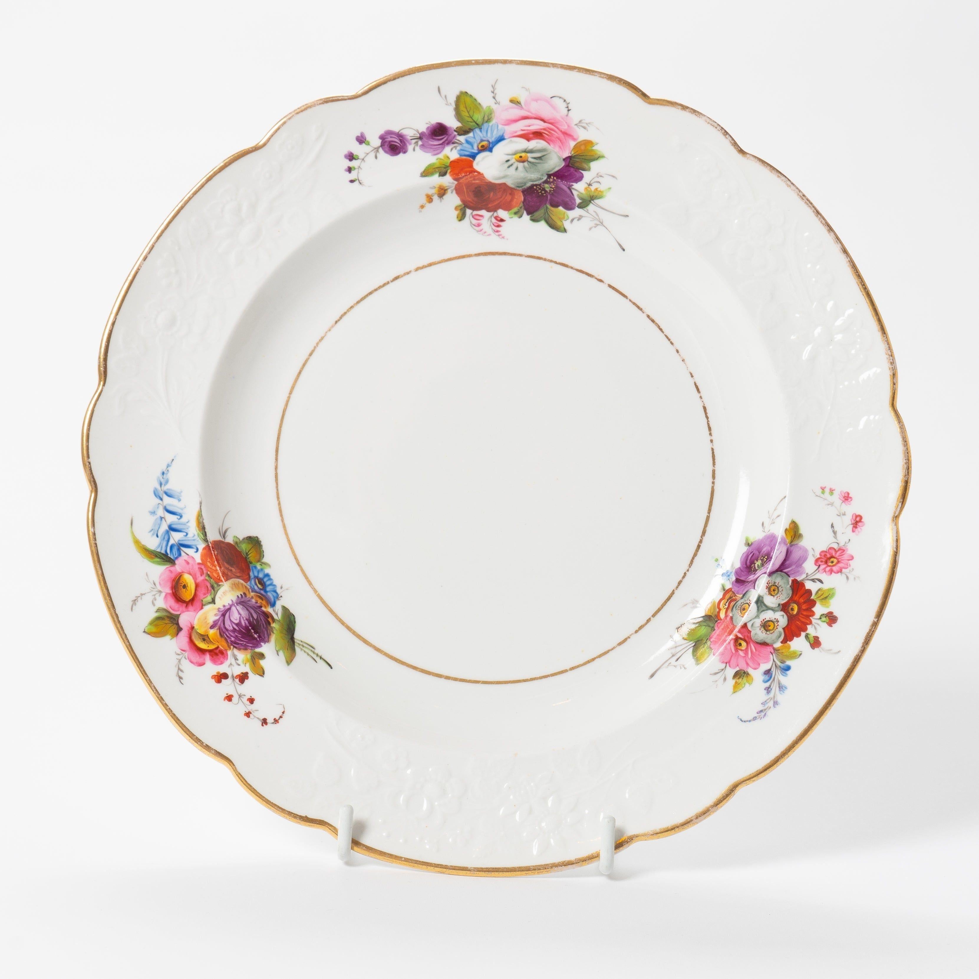 Set of twelve Spode bone china dinner plates with characteristically English hand painted mixed floral bouquets in vivid polychrome enamels. The plates have a scolloped rim and three raised molded floral elements in the border between three bouquets