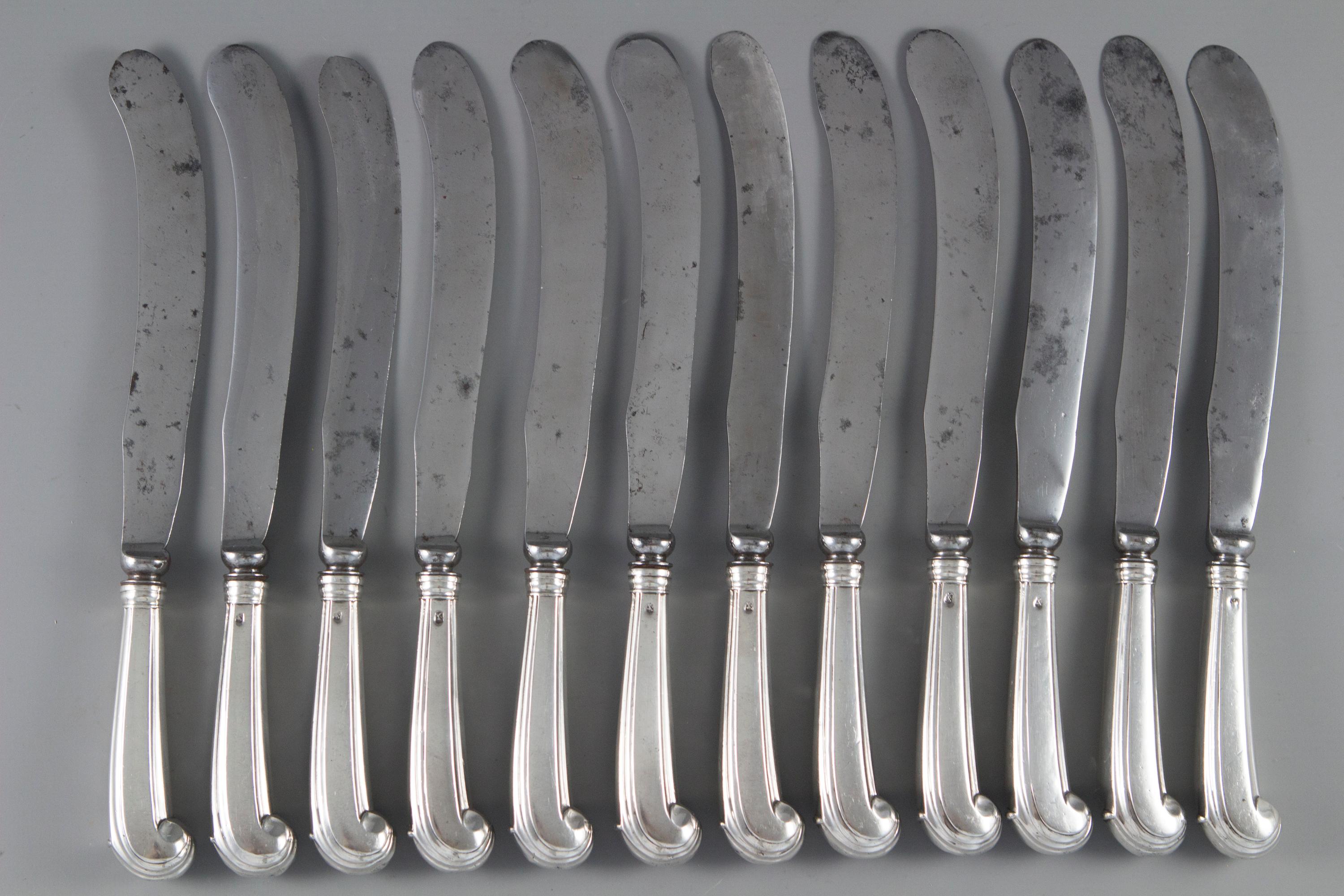 A very rare set of 12 early 18th century table knives. Pistol grip silver hafts with Queen Anne period scimitar shaped blades, the hafts are engraved with a crest of a hand holding a quill.

Hallmarked with the Lion Passant only, some with a