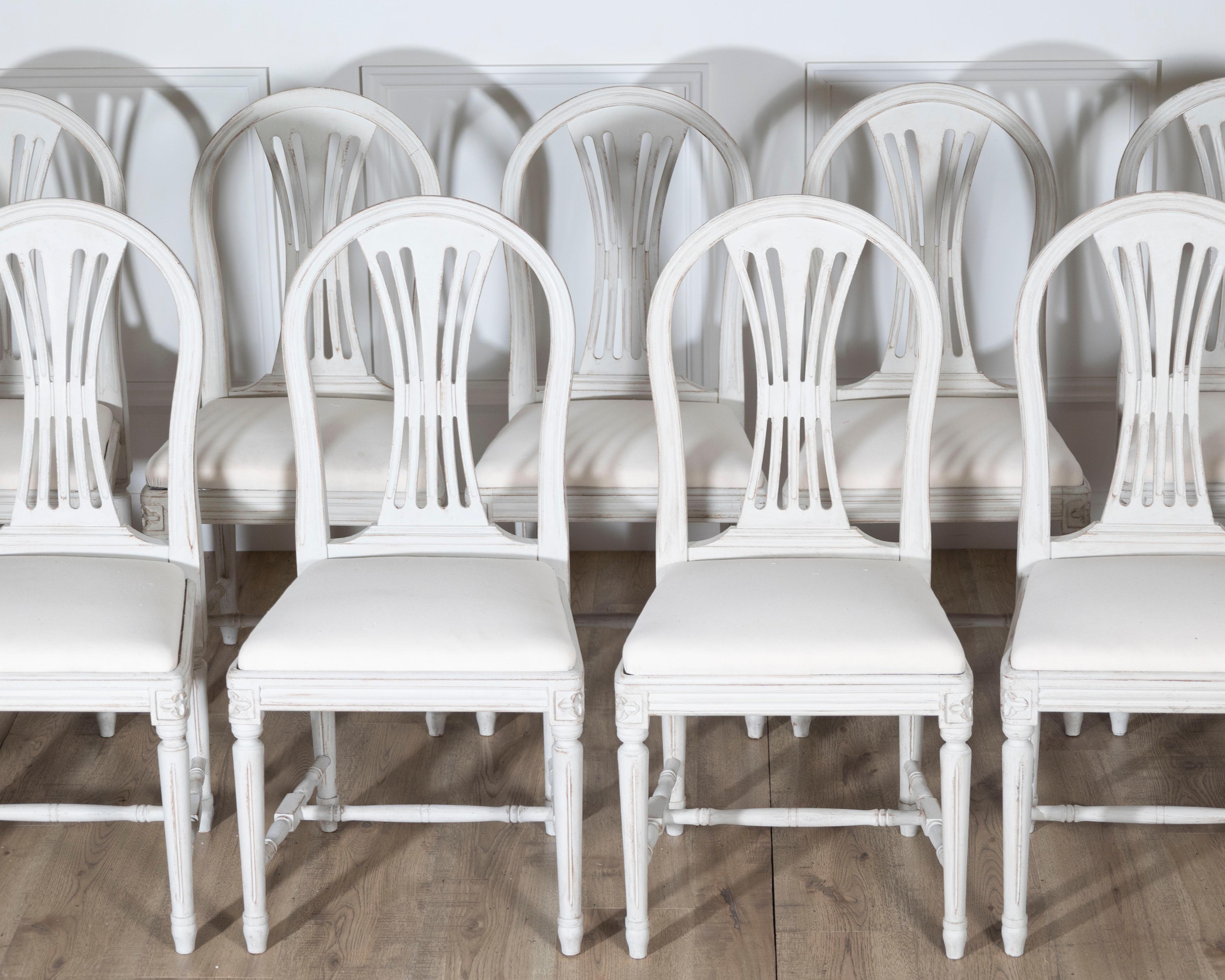 A graceful set of 12 Swedish Gustavian style dining chairs, crafted in the early 20th century and showcasing the clean lines and restrained ornamentation characteristic of the neoclassical Scandinavian aesthetic. Each chair features an arched