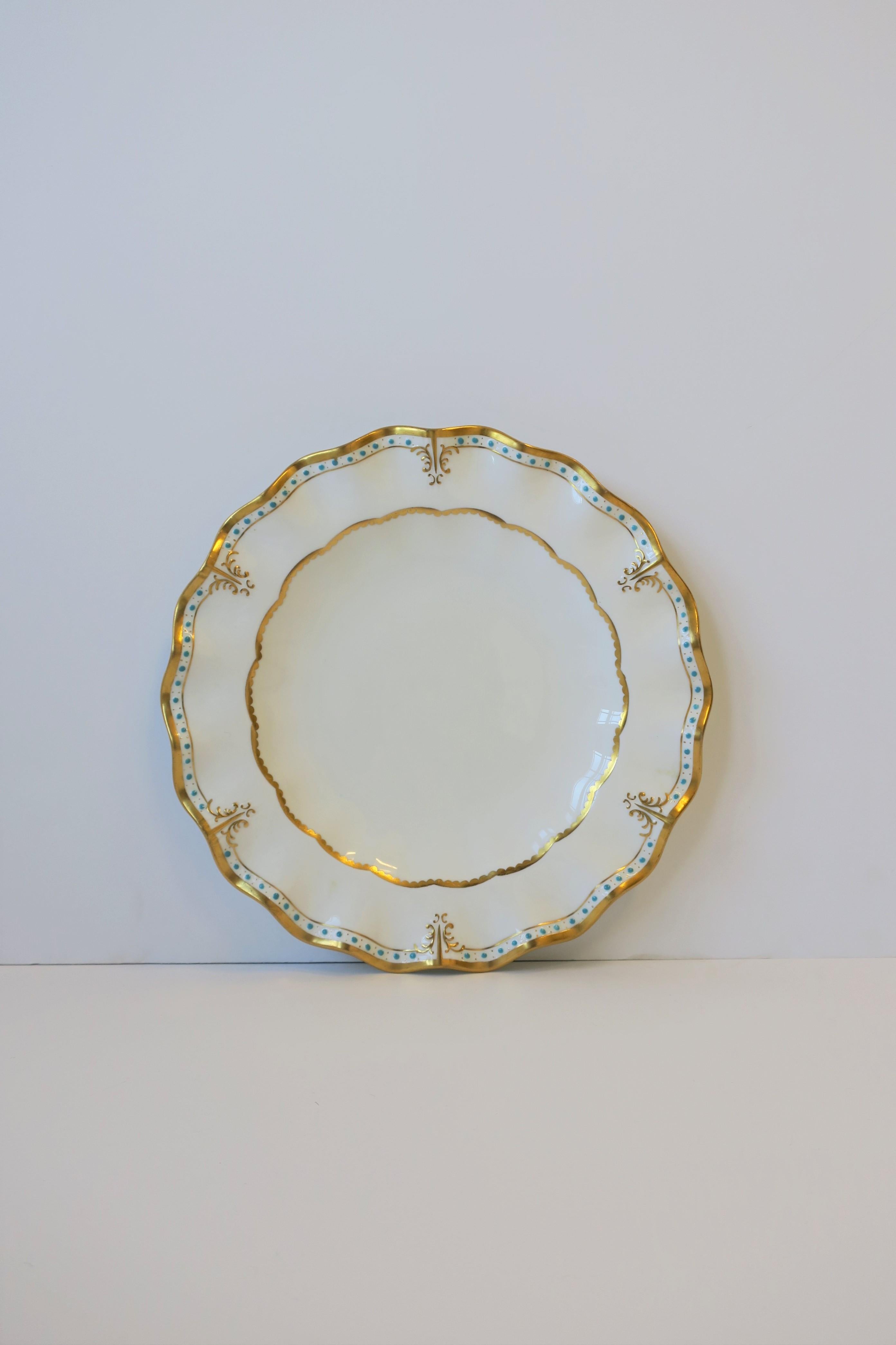 A beautiful set of 12 English 'fine bone china' porcelain dinner plates made by Royal Crown Derby, circa late 20th century, England. Plates are decorated with a 22-karat gold design and small turquoise blue dots - both raised, on an all white