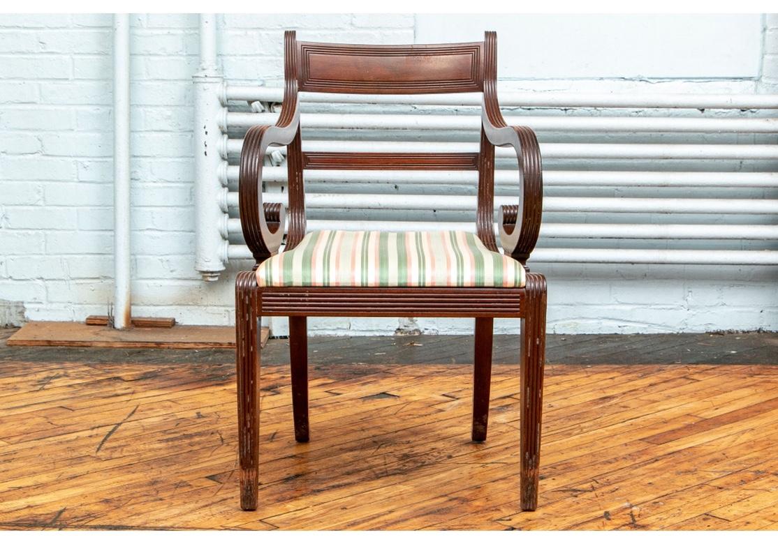 Set of 12 Regency dining chairs, 1820, two-arm and ten side chairs. With heavy ribbed carved frames and Classic fine form. Square tapering front legs and splayed back ones. The seats with newer upholstery in a cream, green and peach striped fabric.