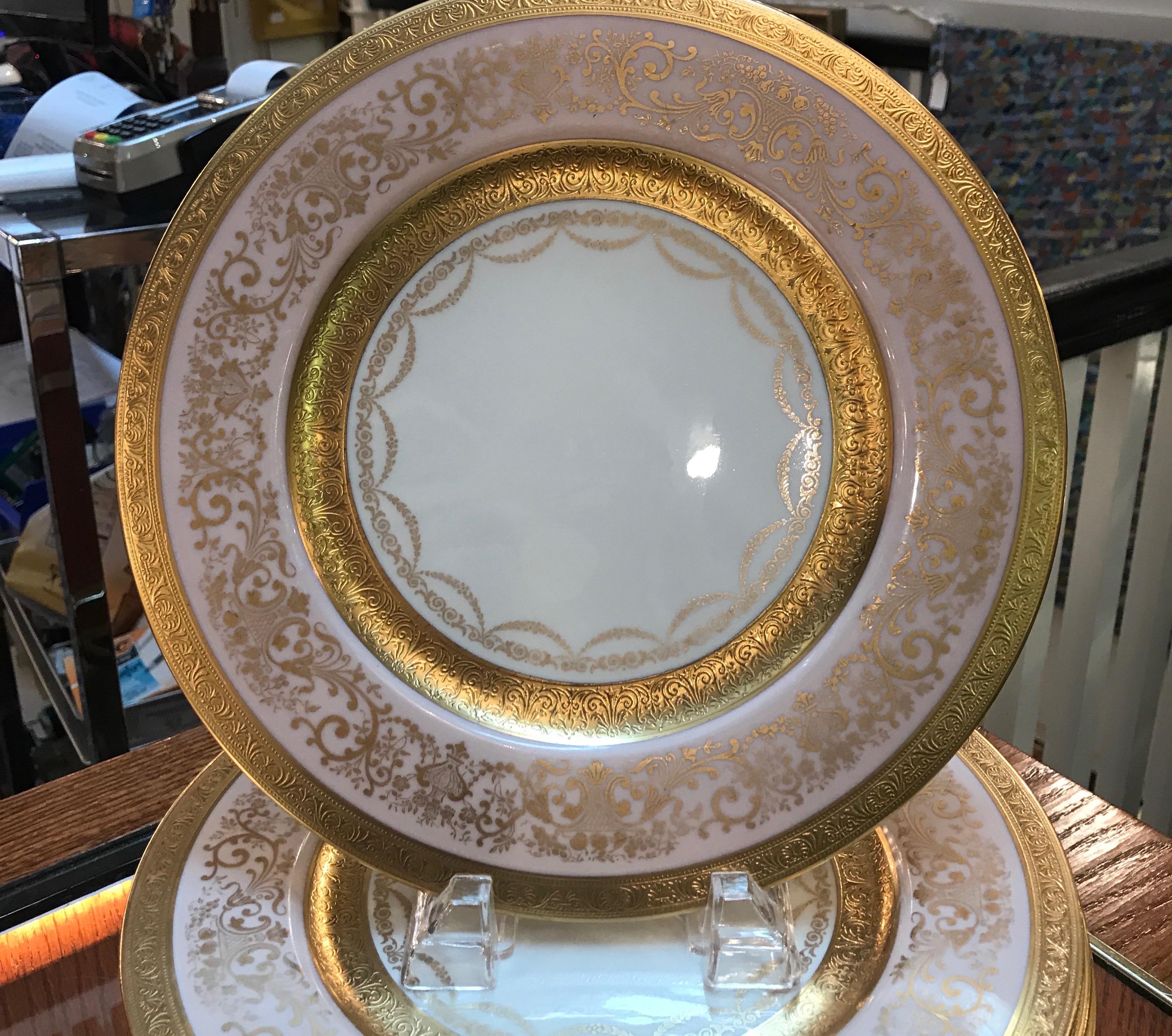 Elegant and formal gold decorated service plates with a pale pink border. The broad pink border with inner and outer gold band with gold scrolling detail with a swaged ring around the center white surface. Made by Rosedale.