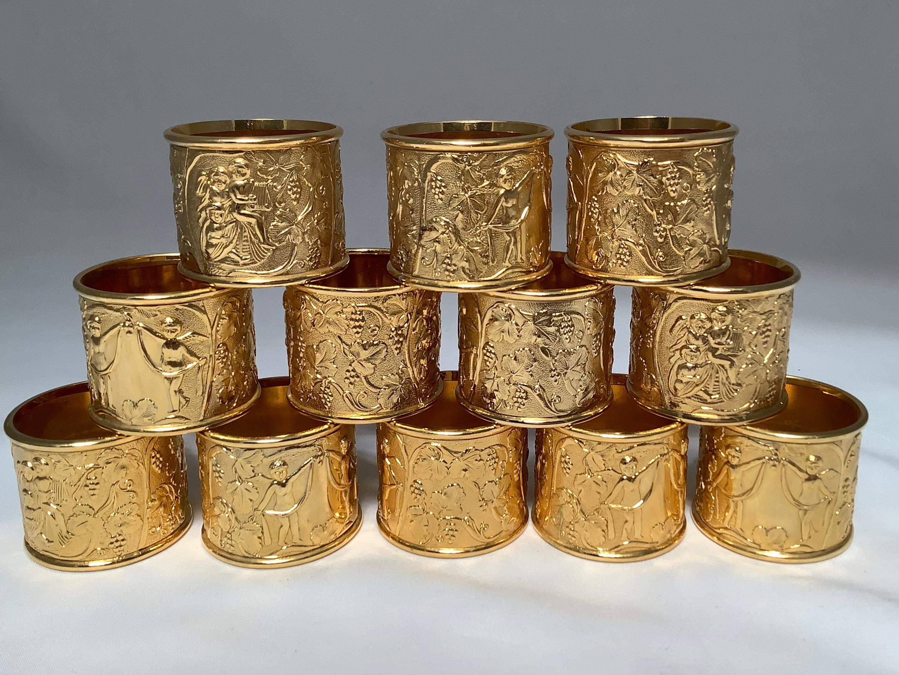 Set of twelve gold plated napkin rings. The beautifully cast napkin rings depict angels with swags and fruits and foliage throughout.