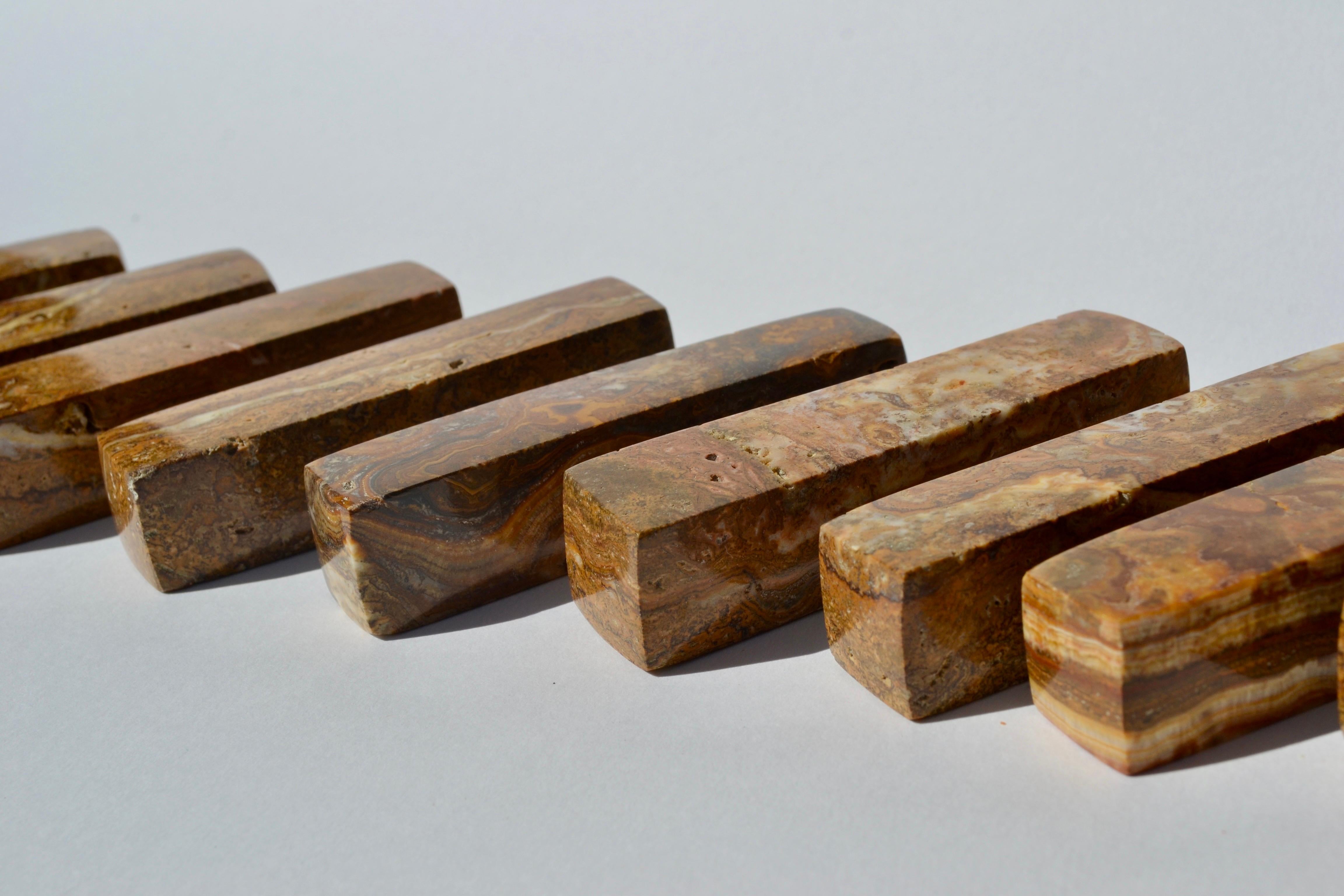 Elegante juego de 12 apoyacuchillos paralelepípedos de travertino dorado bruñido, de la década de 1970, fabricados en Francia. Cada pieza está tallada en travertino dorado de tonos cálidos con vetas naturales, ofreciendo un aspecto crudo y
