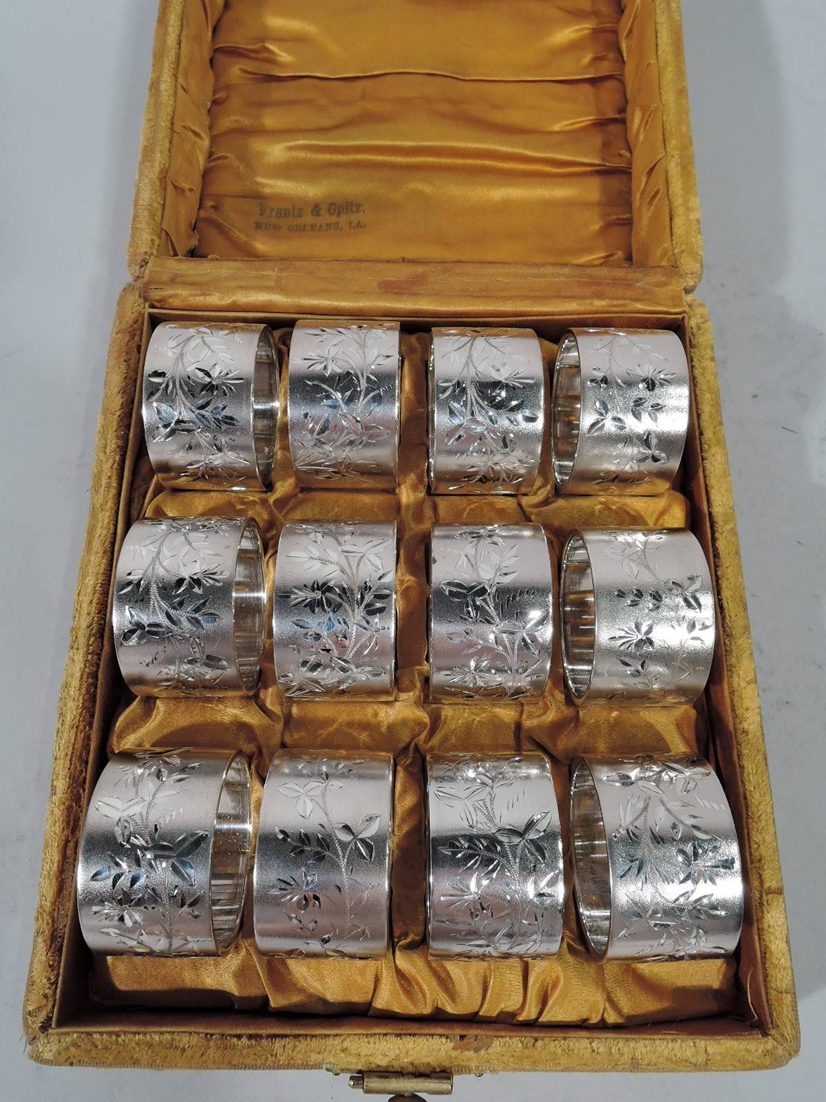 Set of 12 aesthetic sterling silver napkin rings. Made by Gorham in Providence, circa 1880. Each: Bright-cut stylized blossoming branch on butler finish. Stylistically coherent with minor variations. Engraved script monogram. Hallmark includes no.