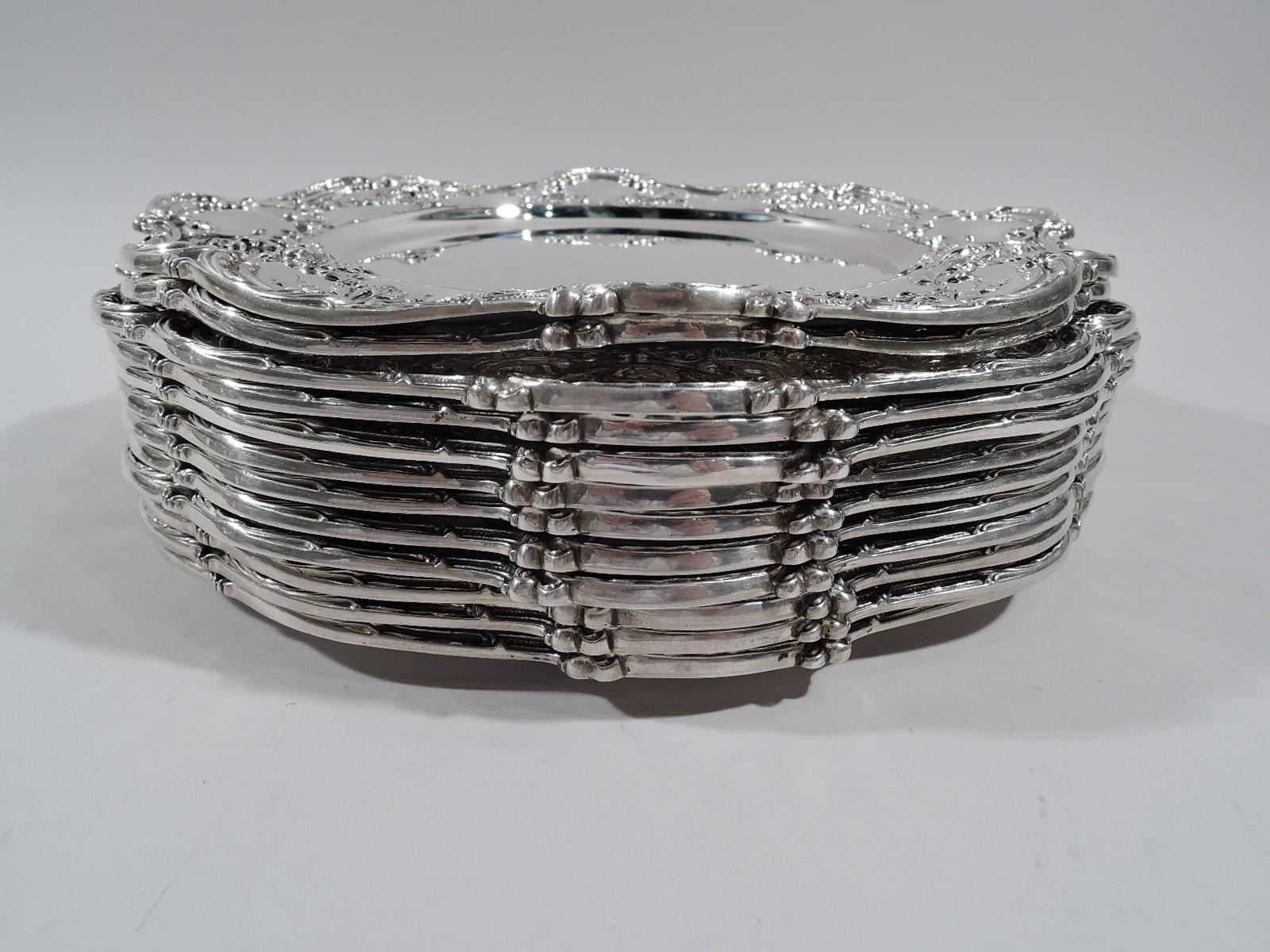 Set of 12 Edwardian Rococo sterling silver dinner plates. Made by Gorham in Providence. Each: Round well and scrolled rim. Shoulder has chased garlands alternating with scrolled frames (vacant). Fully marked including no. A6602. Two plates have 1907