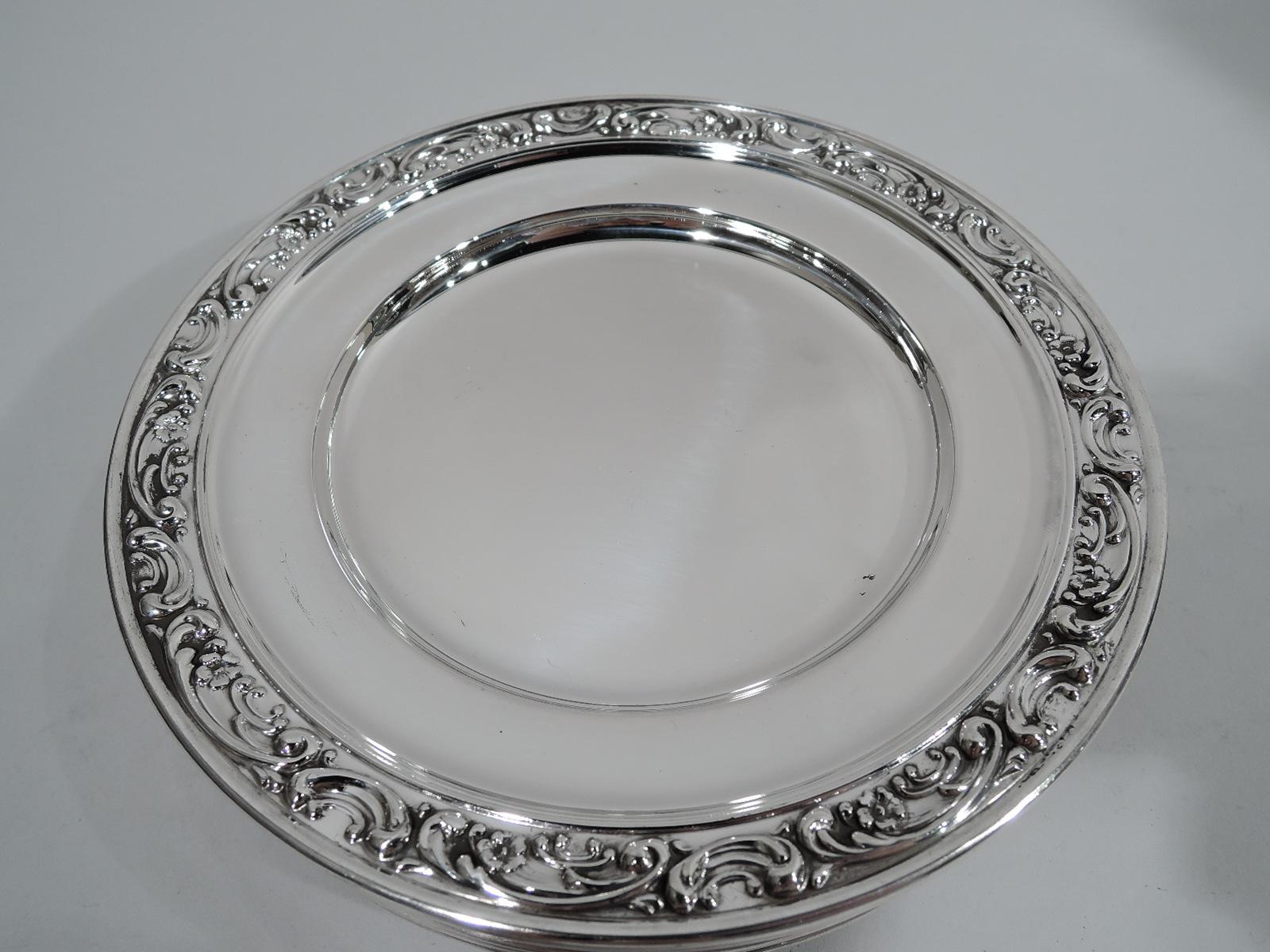 Set of 12 rose scroll sterling silver bread and butter plates. Made by Gorham in Providence. Round well and plain shoulder. Rim has chased scrolls and flower heads between molded borders. Fully marked and numbered 1234. Total weight: 39.5 troy