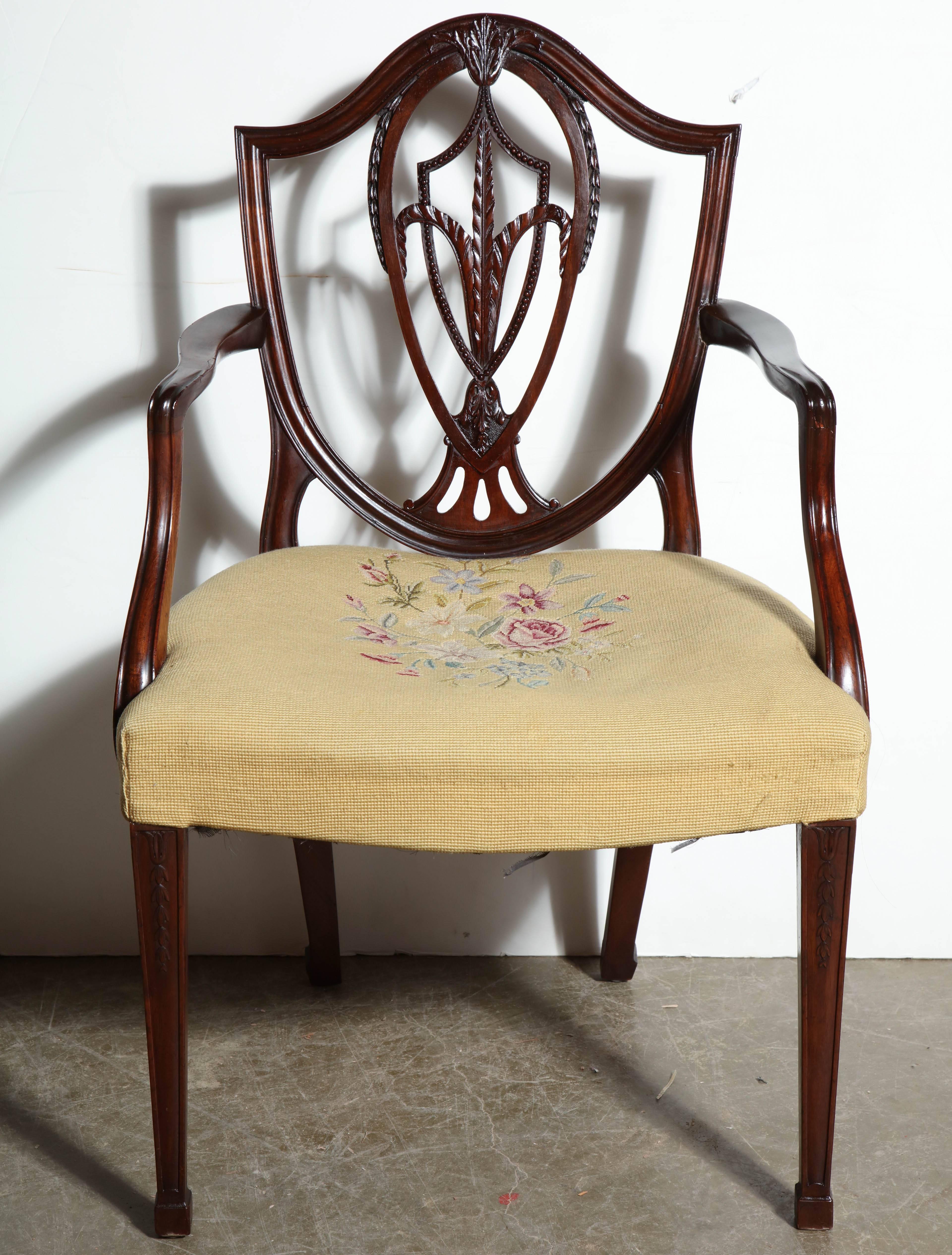 Set of 12 George III (Hepplewhite) mahogany shield back dining chairs with carved interlaced splats, molded arms, spade feet and needlepoint upholstered seats.

The set is comprised of 12 armchairs.