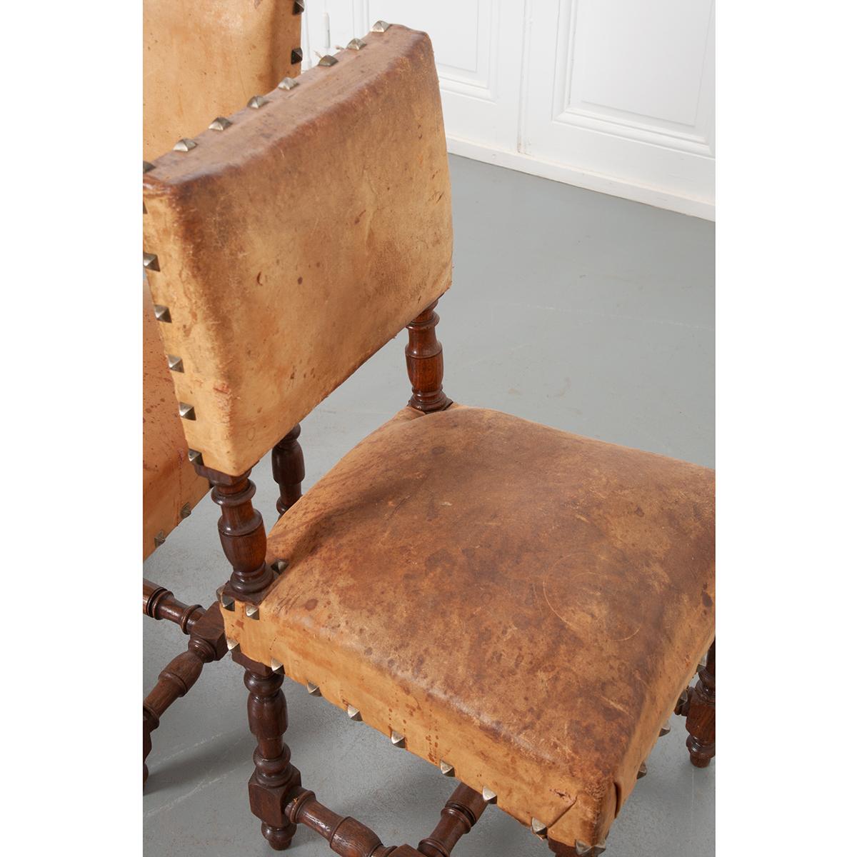 This set of twelve dining room chairs retains its original leather upholstery that’s been perfectly aged and feels soft to the touch. Both the seat and chair back are padded for comfort and fixed with large decorative nail heads that stand out