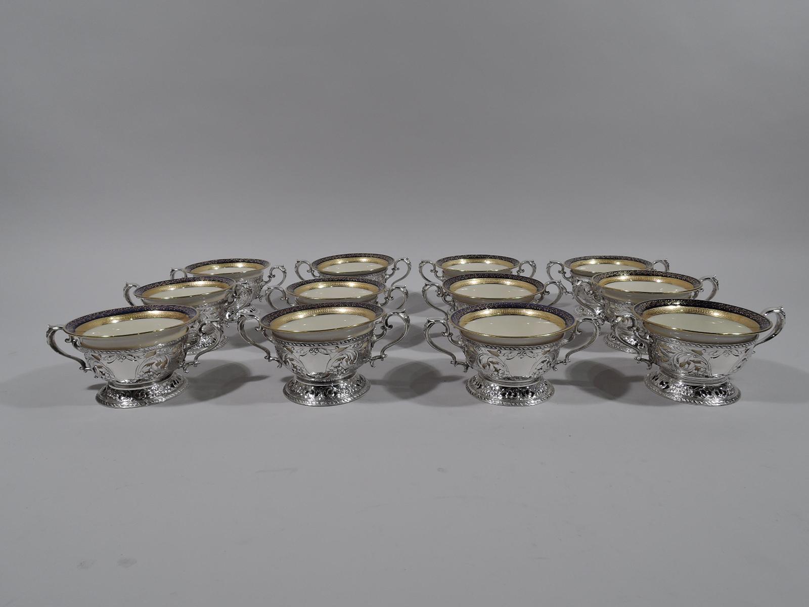 Set of 12 sterling silver bouillon bowl holders. Made by Gorham in Providence, circa 1900. Each: Curved sides with open bottom, raised spread foot, and capped high-looping double-scroll handles. Sides have chased leafing scrolls and flowers