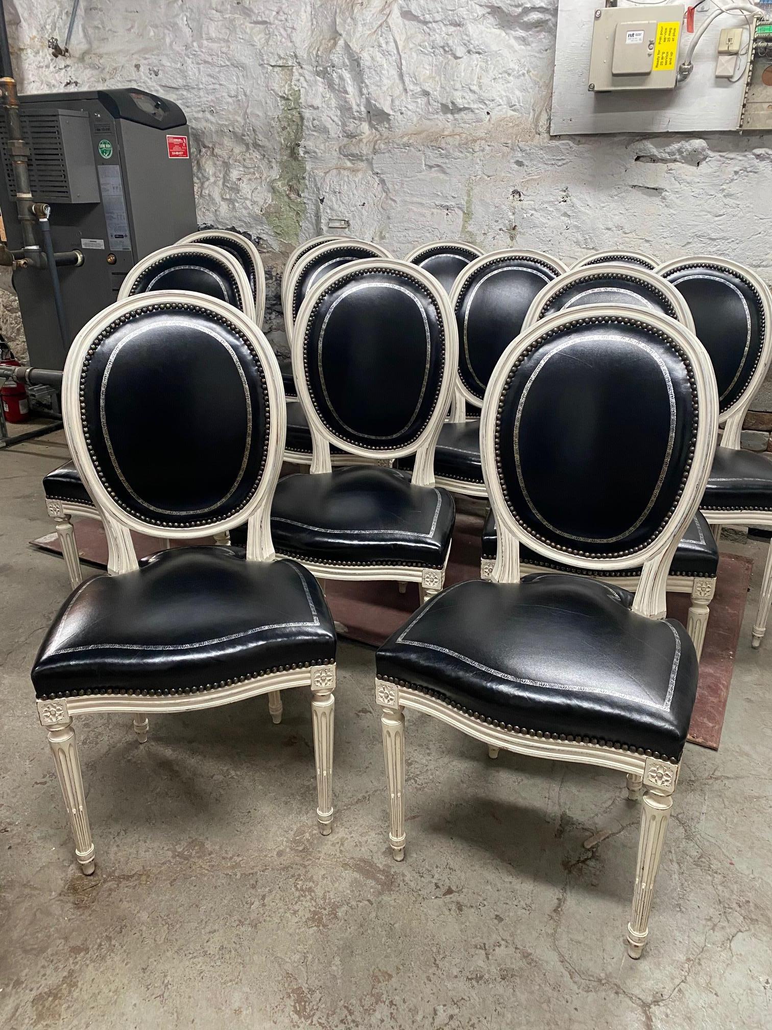 Set of 12 white painted Louis XVI style dining chairs in the manner of Maison Jansen with black leather tooled silver design.