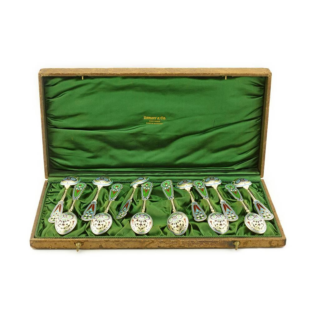 An antique Imperial Russian era set of twelve gilded silver, champlevé, guilloché, and plique-à-jour enamel spoons by Imperial Court Jeweler Khlebnikov of Moscow, retailed by Tiffany & Co., Moscow, 1908-1917. The group of 12 spoons decorated as a