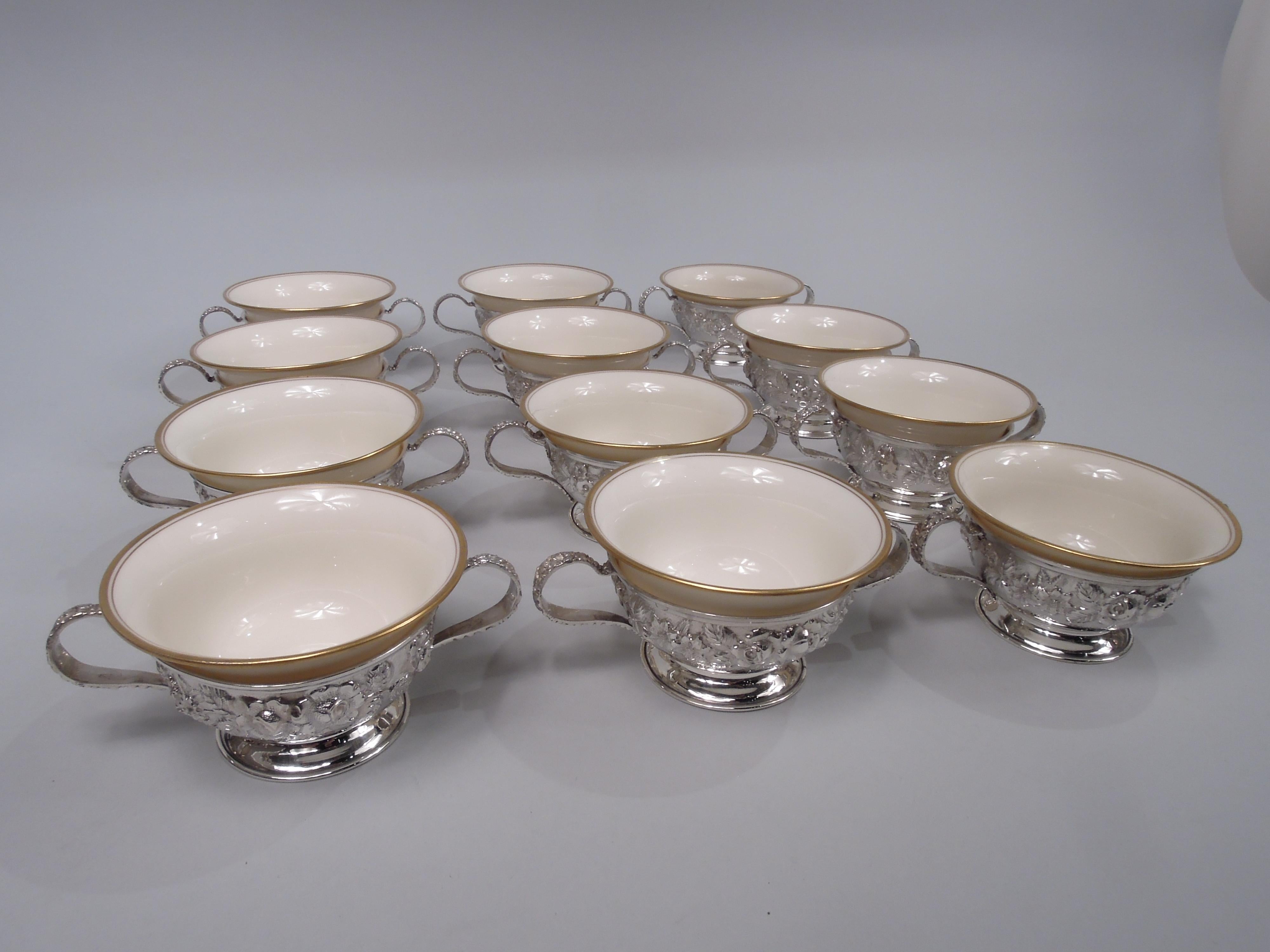 Set of 12 Edwardian sterling silver holders. Made by Schofield in Baltimore, ca 1910. Each: Round and curved bowl with floral repousse; open bottom and plain spread foot. High-looping side handles with case repousse-style floral ornament. With: