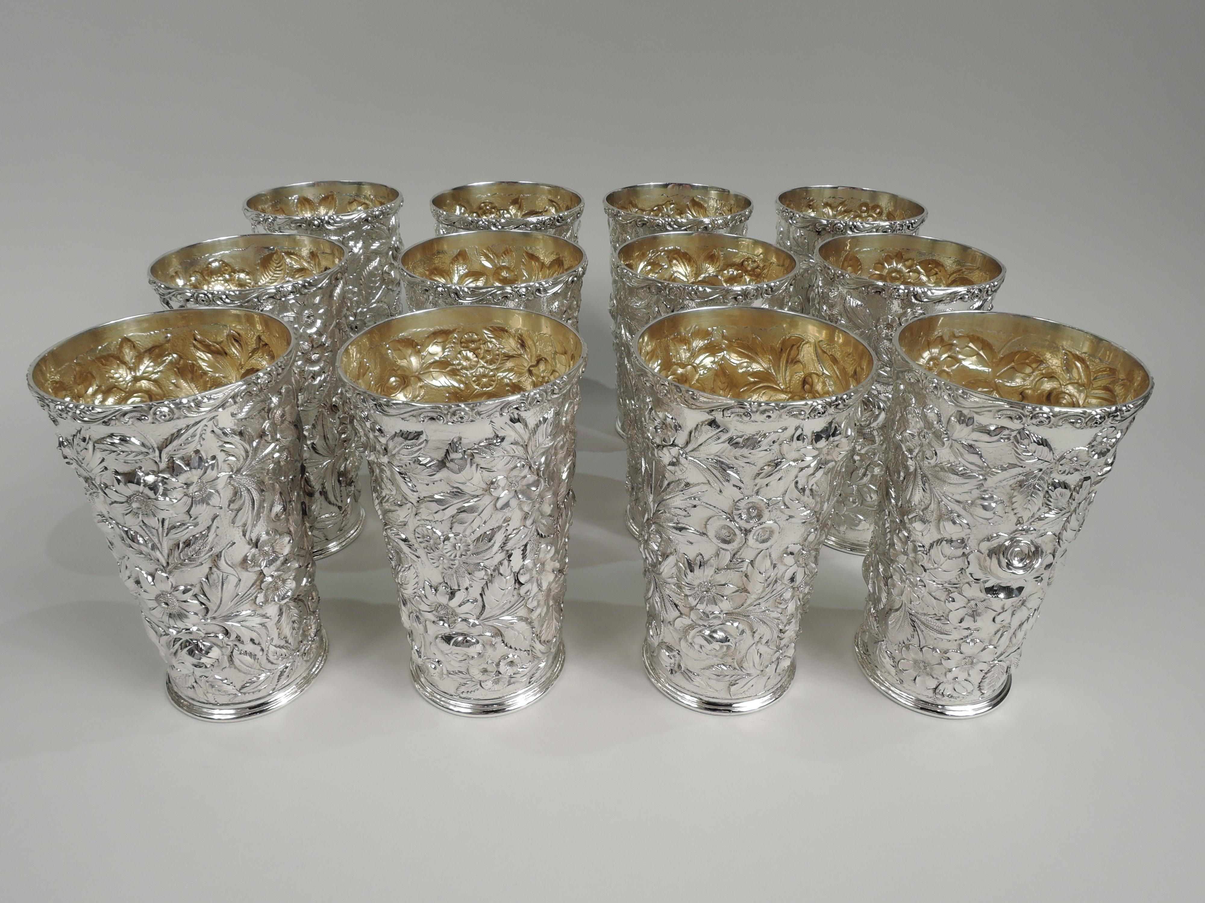 Set of 12 Edwardian sterling silver highballs. Made by Heer-Schofield Co. in Baltimore, ca 1910. Each: Straight and tapering sides with floral repousse. Applied tooled scrolled rim and plain and stepped foot. Gilt washed interior. Pretty and tactile