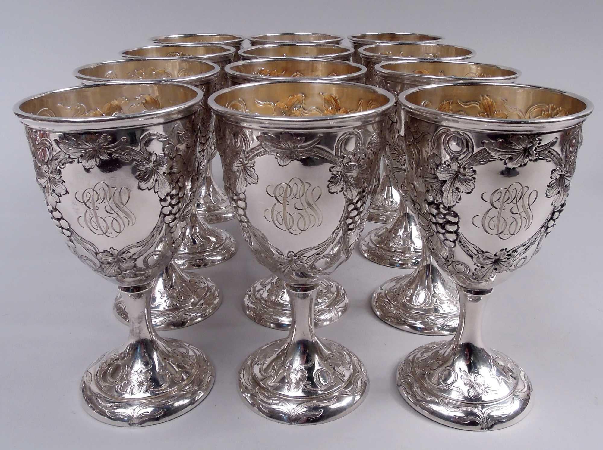 Set of 12 Edwardian sterling silver goblets. Made by Schofield in Baltimore, ca 1910. Ovoid bowl on stem flowing into raised foot. Meandering and whiplash fruiting grapevine forming round frame engraved with interlaced script monogram. Bowl interior