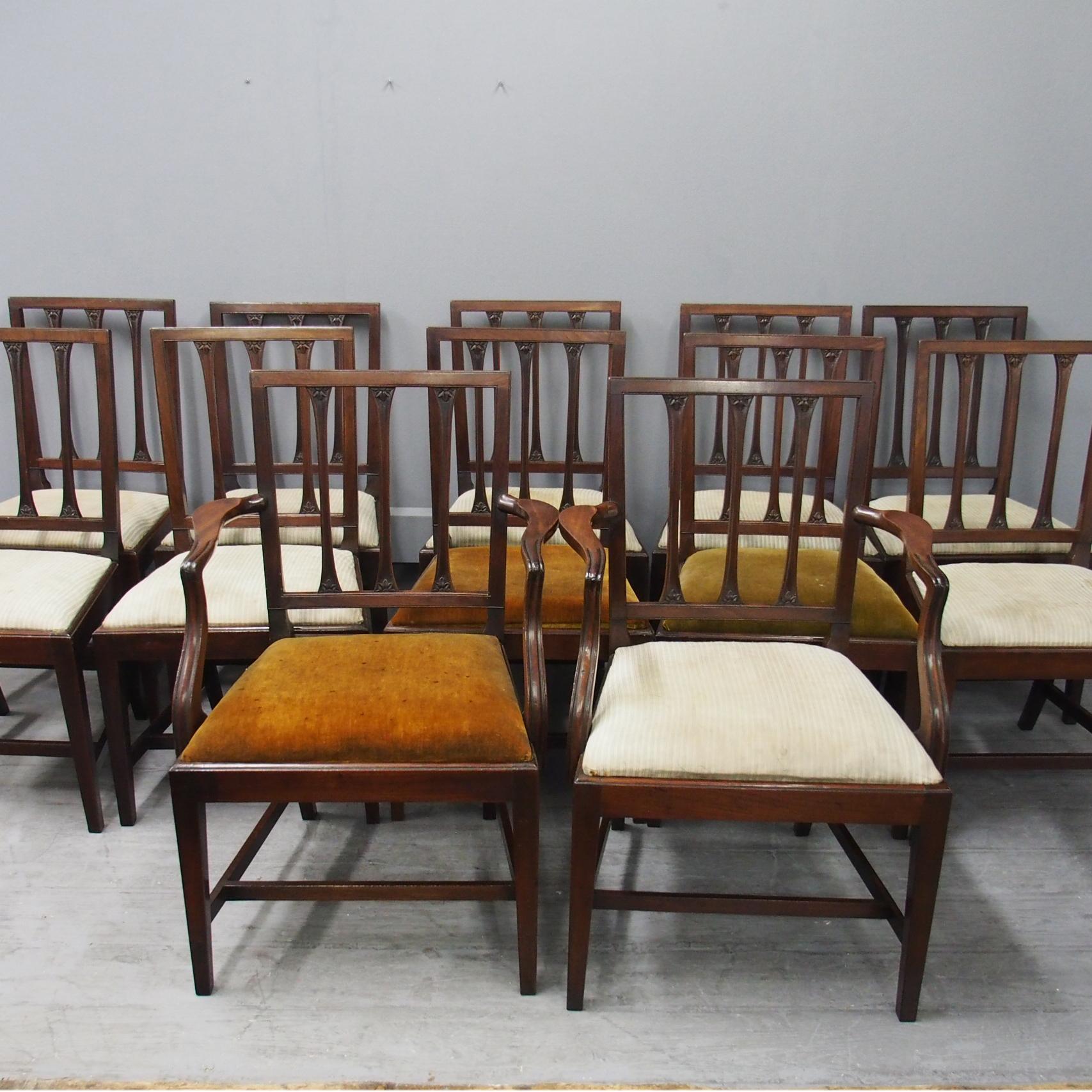 Rare original set of 12 (10 +2) Scottish George III mahogany dining chairs with Sheraton influence, circa 1780. The narrow reeded top rail is supported by 3 narrow splats with flared and foliate carved ends, leading on to outswept arms over