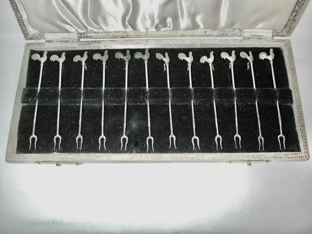 Set of 12 silver cockerell cocktail sticks dated 1929/30, Assayed In Birmingham.
Made by Alexander Scott.
These cocktail sticks have cast cockerells and the pitchfork shaped ends,
 really grip the olive or marachino cherry.
The box is original,