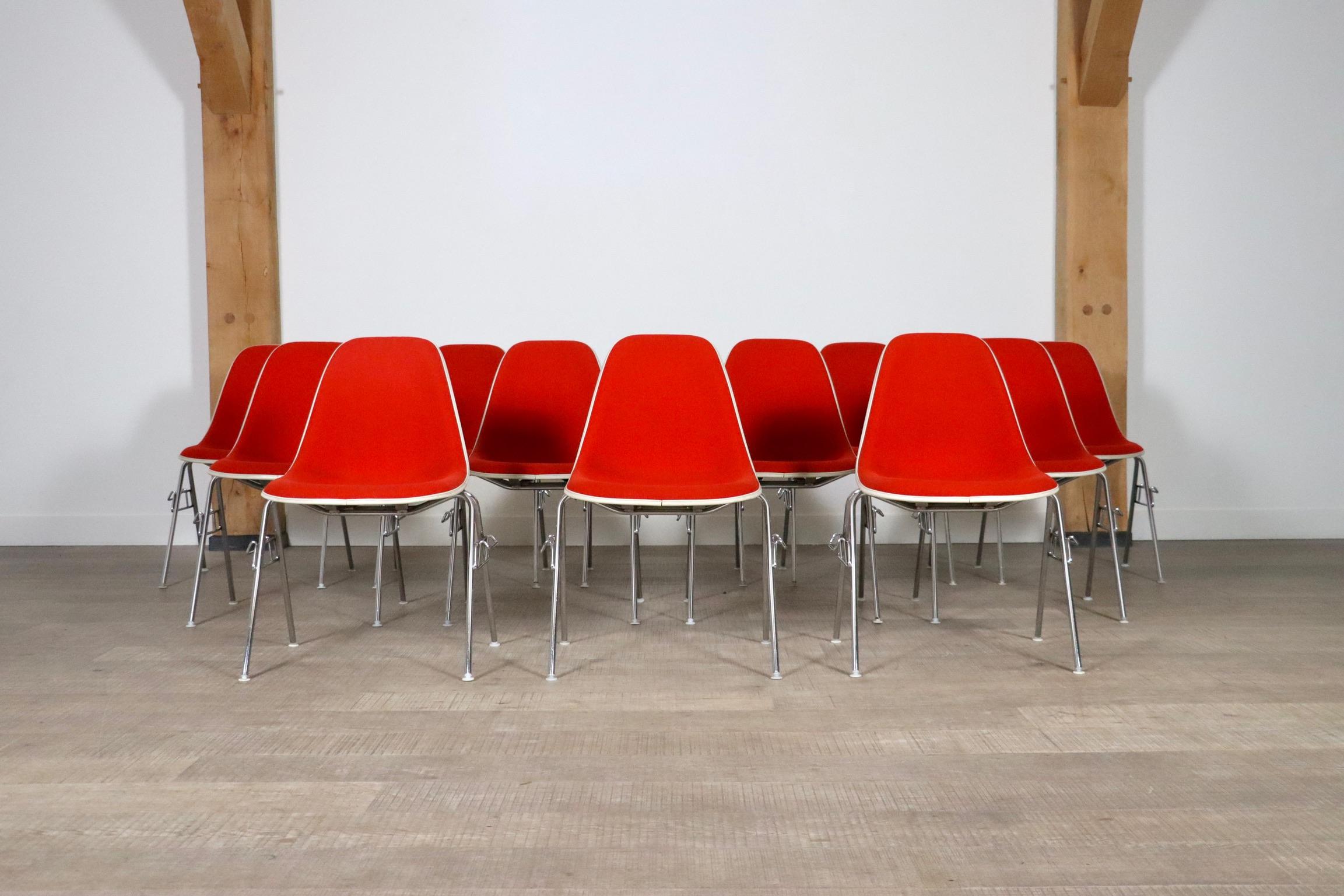Nice set of 12 stackable chairs model DSS by Charles and Ray Eames for Herman Miller. This set is made from a fiberglass shell and is upholstered in red with a white edge. A nice set which can be easily stacked and stored if needed, making it a nice