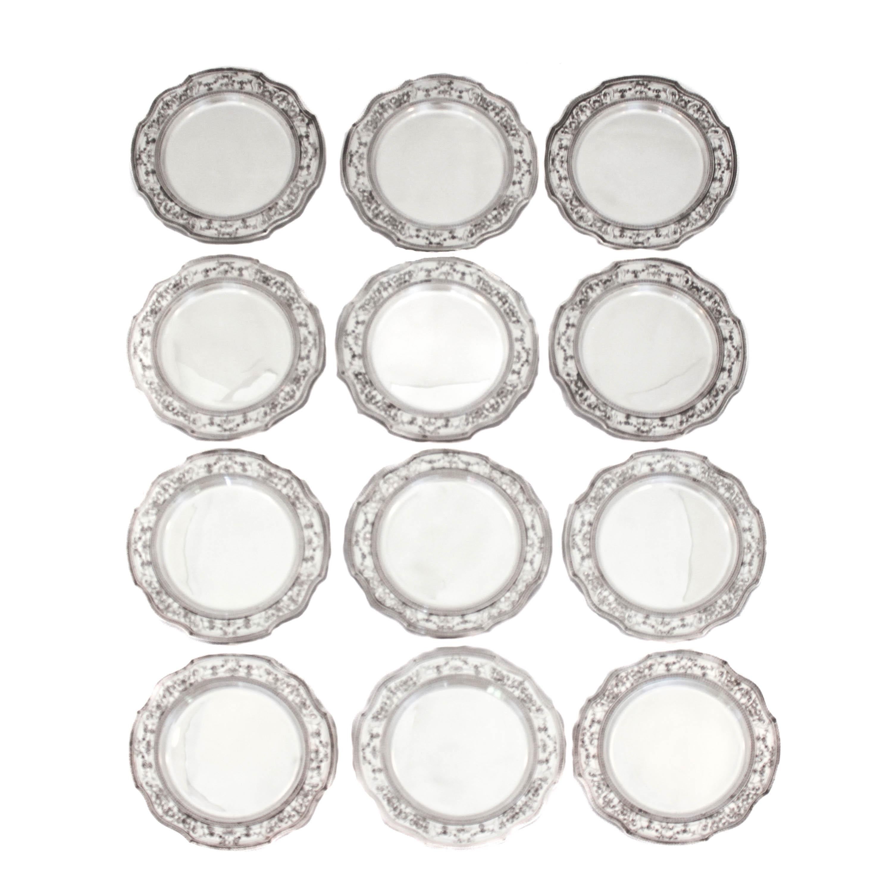 Se ofrece un juego completo de doce platos de pan de International Silver.  La elaboración es exquisita y el detalle incomparable.  El borde está festoneado y todo el contorno está cincelado; coronas, flores y remolinos se unen para crear un motivo