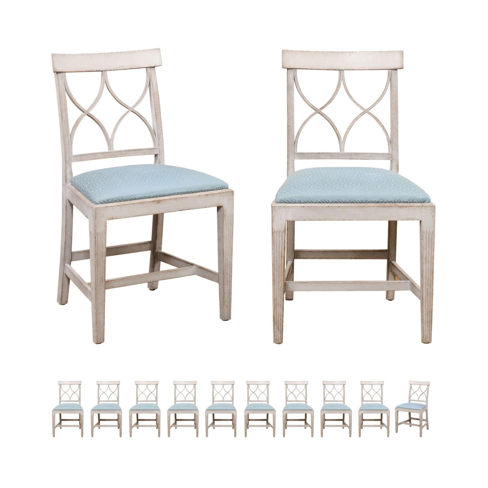 A set of 12 Swedish dining room side chairs from the early 20th century, with new upholstery. Created in Sweden during the early years of the 20th century, each of this set of side chairs features an open back pierced with sinuous motifs and topped