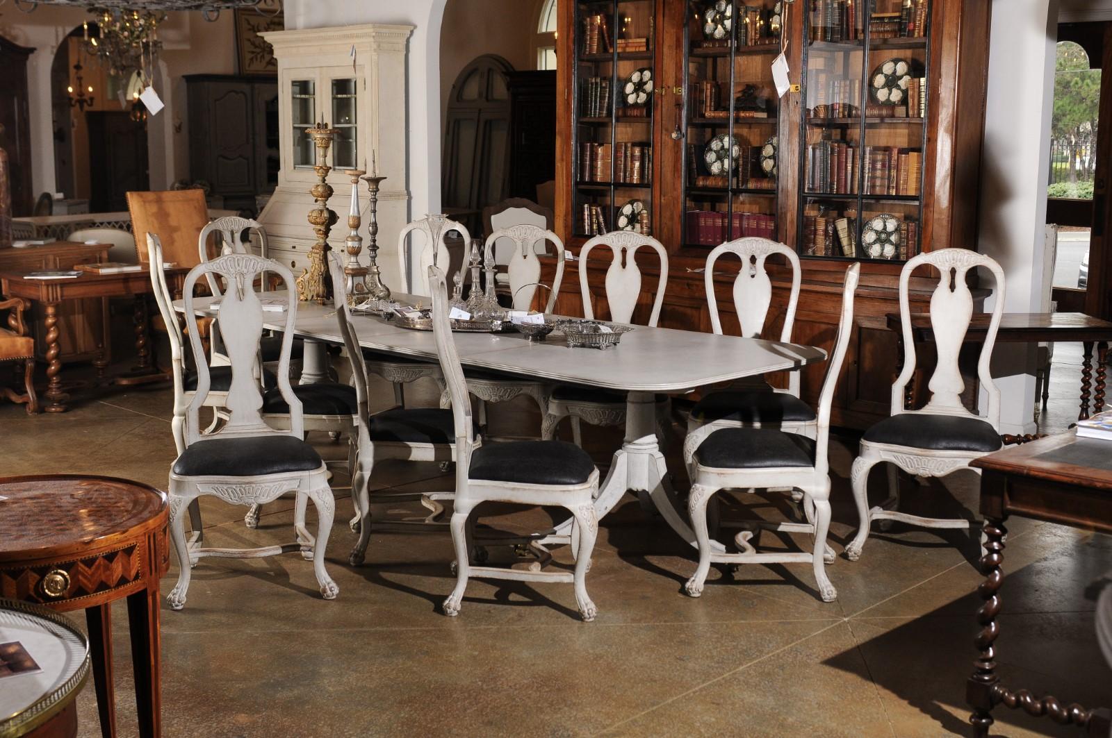 A set of 12 Swedish Rococo style painted wood high back dining chairs from the 19th century, with black upholstered seats, carved pierced splats, cabriole legs and cross stretchers. Created in Sweden during the 19th century, each of this set of 12