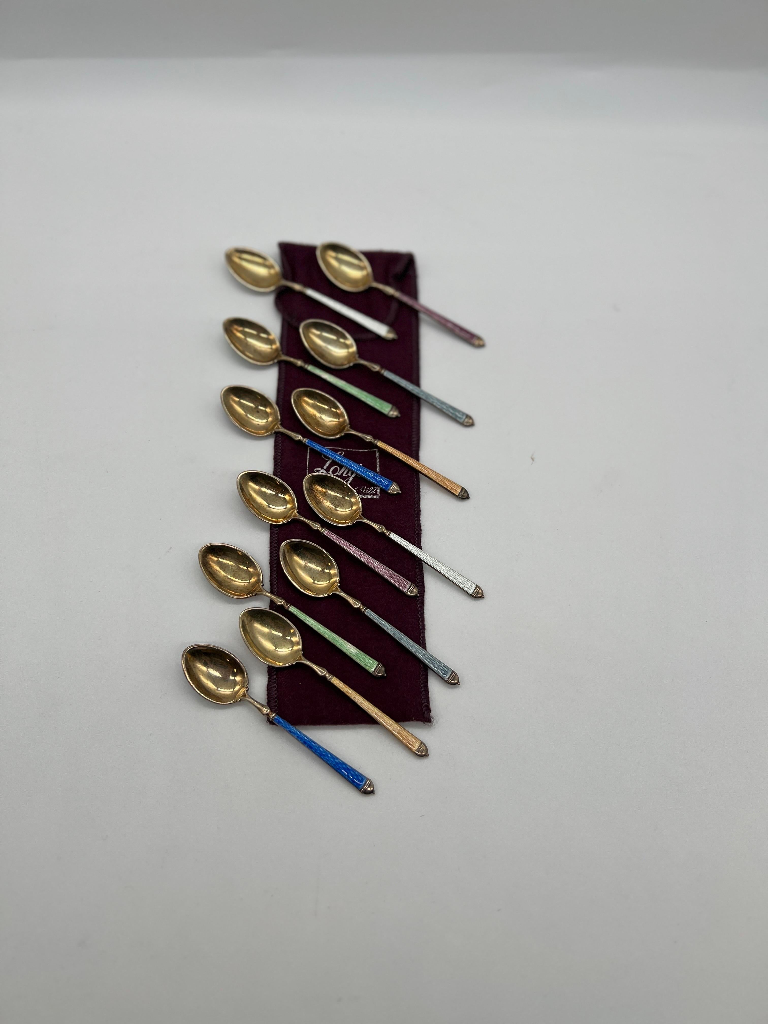 The Thomae Company (American, founded 1920), circa mid 20th century.

A fine grouping of 12 sterling silver demitasse spoons in 6 different color enamels, cobalt, orange, green, light blue, white and purple. The bowls of each spoon have a gold gilt