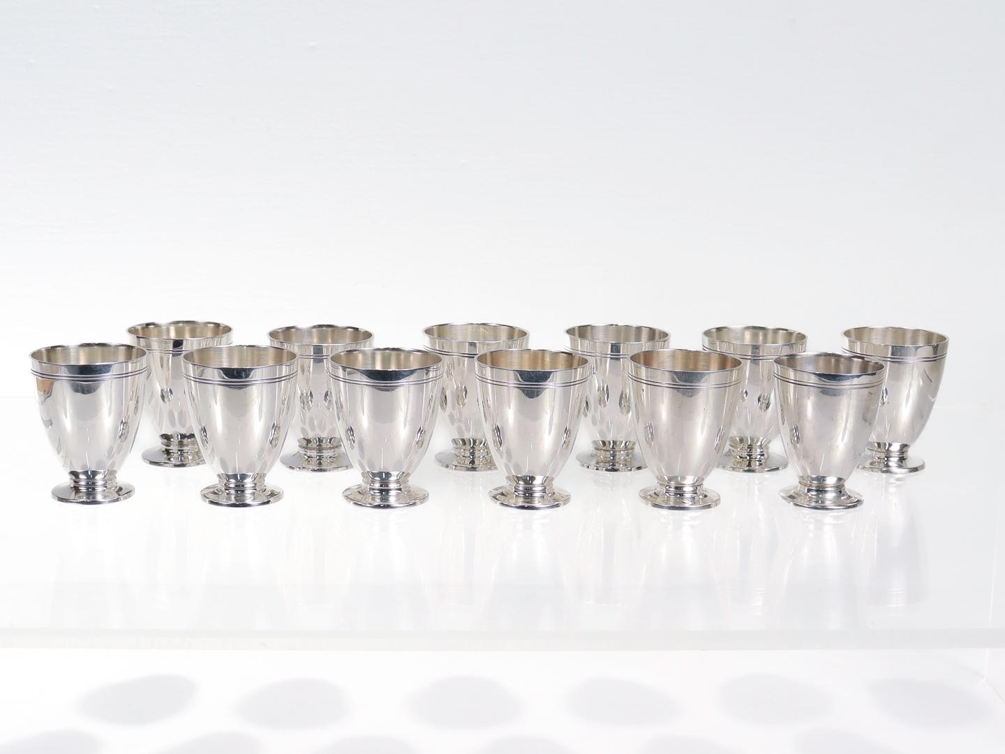 A fine set of 12 silver cordials or shot glasses.

By Tiffany & Co.

In sterling silver.

Each shot cup with terrific streamlined design including a plunger foot, a tapered body, and bold, etched double-line decoration.
.
Marked to the base of each